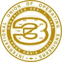 Logo of the International Union of Operating Engineers. It features a golden ring with the words "International Union of Operating Engineers" and "Organized Dec. 7, 1896" encircling a stylized compass with "Labor Omnia Vincit" inside.