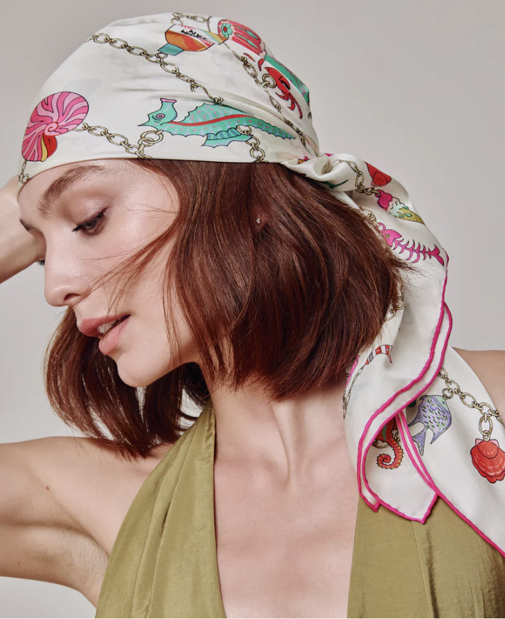 Woman with red hair wearing a patterned silk headscarf and print dress, looking down with her eyes closed. The scarf on her head is from Echo New York