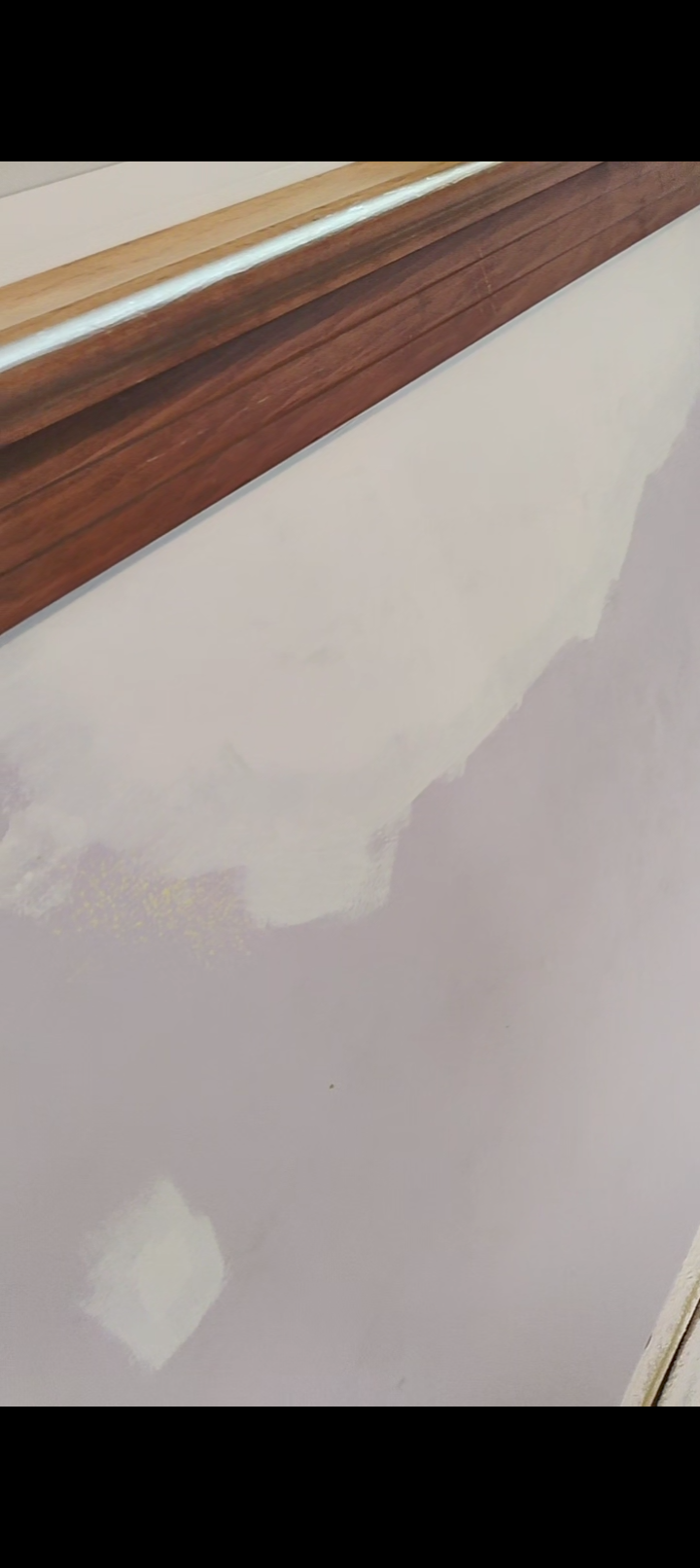Photo of a wall with partially painted drywall, showing a section of unpainted drywall and a baseboard at the top.