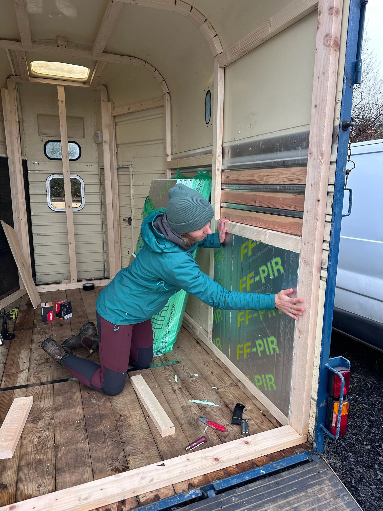 Helena installing insulation panels inside the drift sauna, kneeling on the floor, with various tools and materials around her. the sauna is now a completed Finnish style sauna in Bideford.