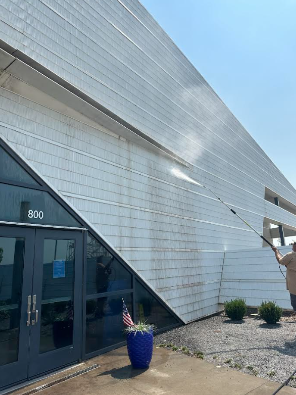 Person pressure washing the side of a modern building with a glass door entrance