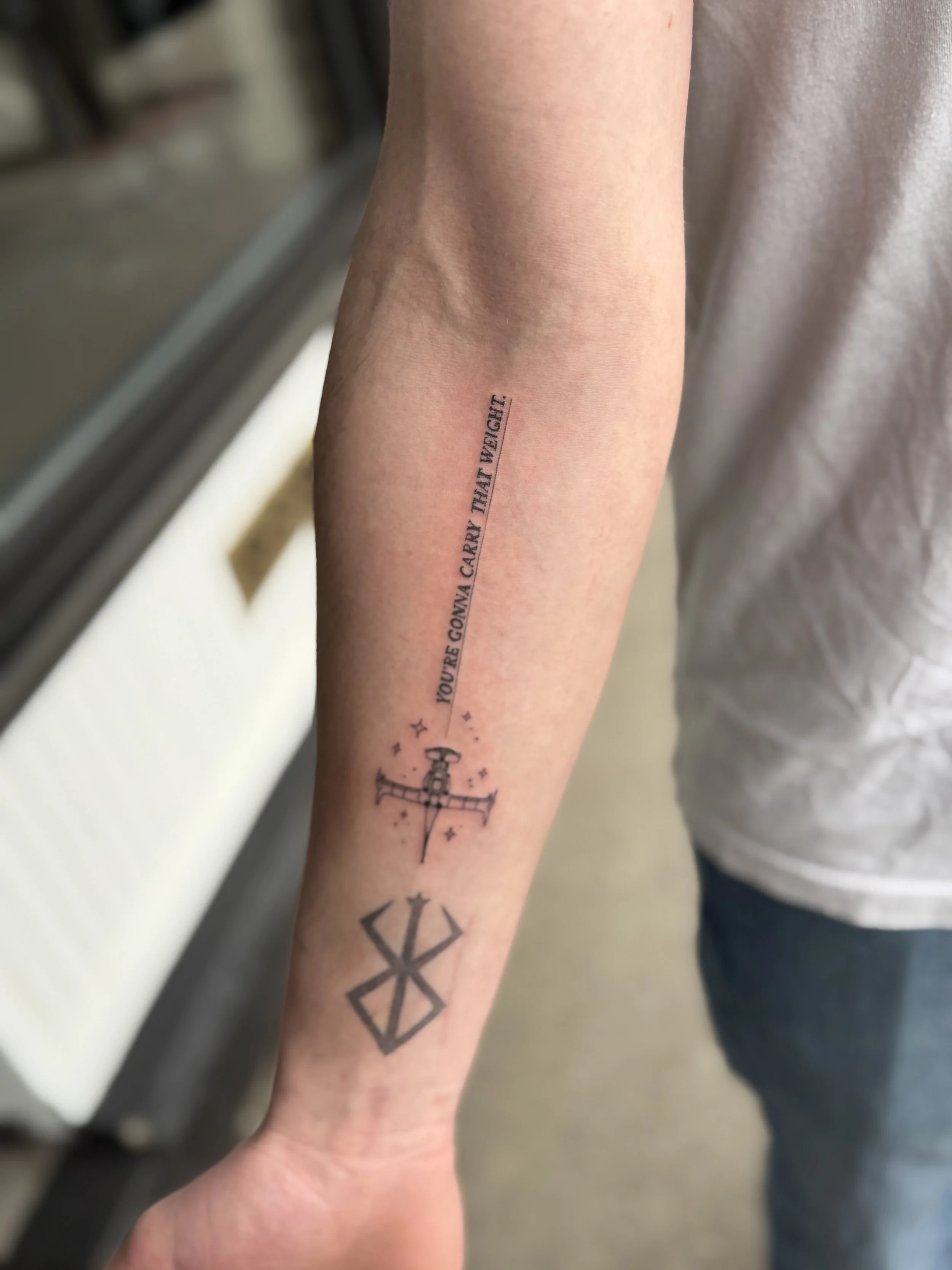 Tattoo of a compass and star on inner forearm, with partial quote 'YOU'RE GOING TO WIN. TRY THAT WEIGHT'.