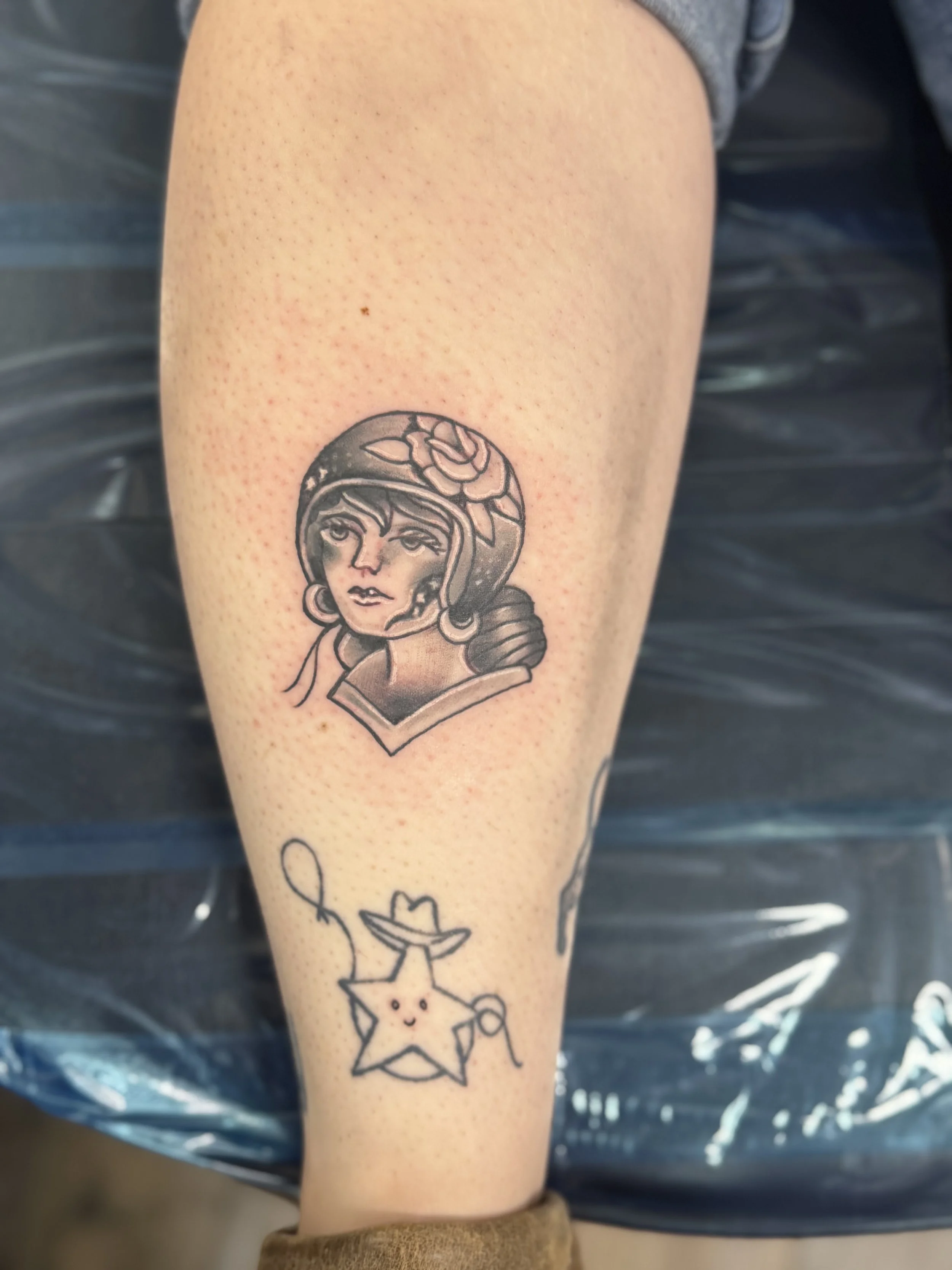 Tattoo of a woman's face with a rose in her hair on person's arm, with additional small star and moon tattoos below.