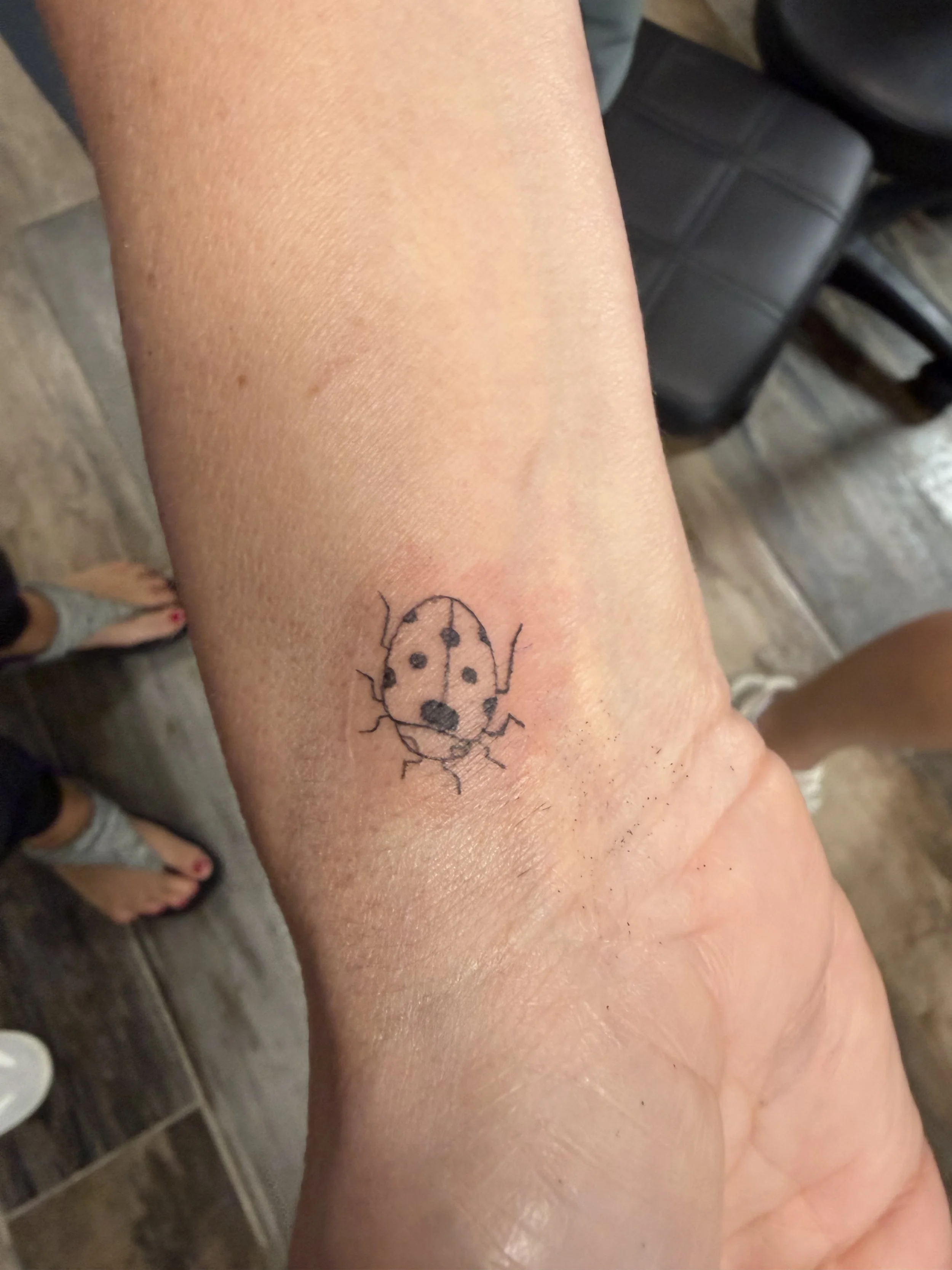 A person's lower leg with a small ladybug tattoo on the skin.
