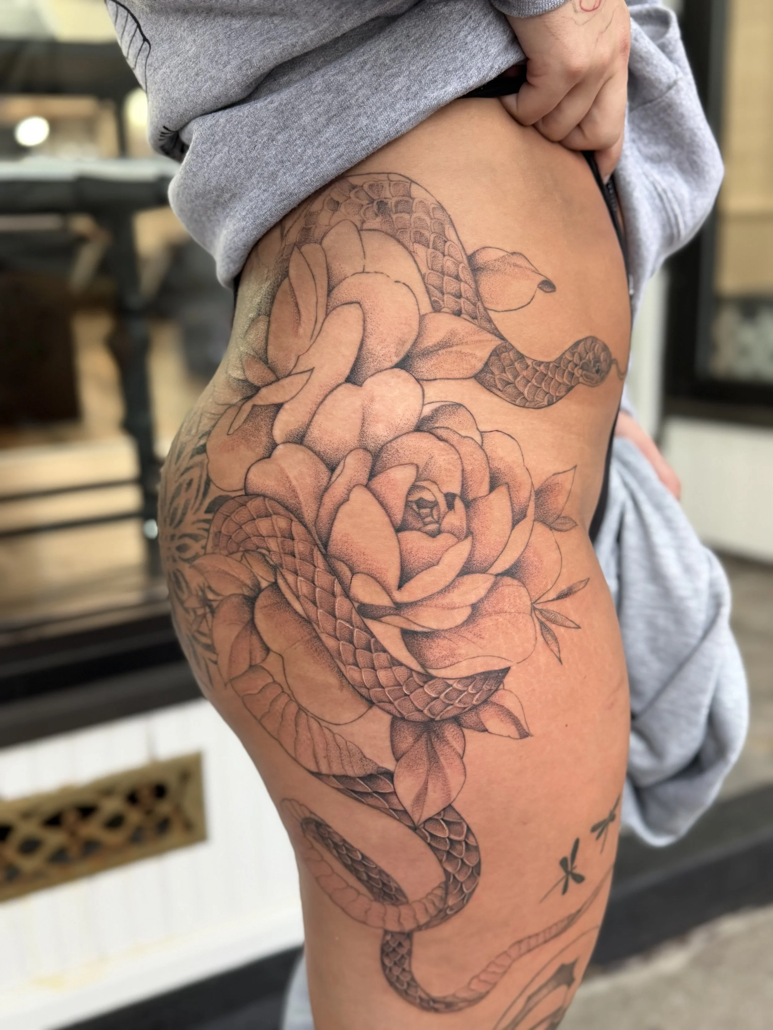 Close-up of a person's thigh with a detailed black and gray tattoo of a snake intertwined with flowers.