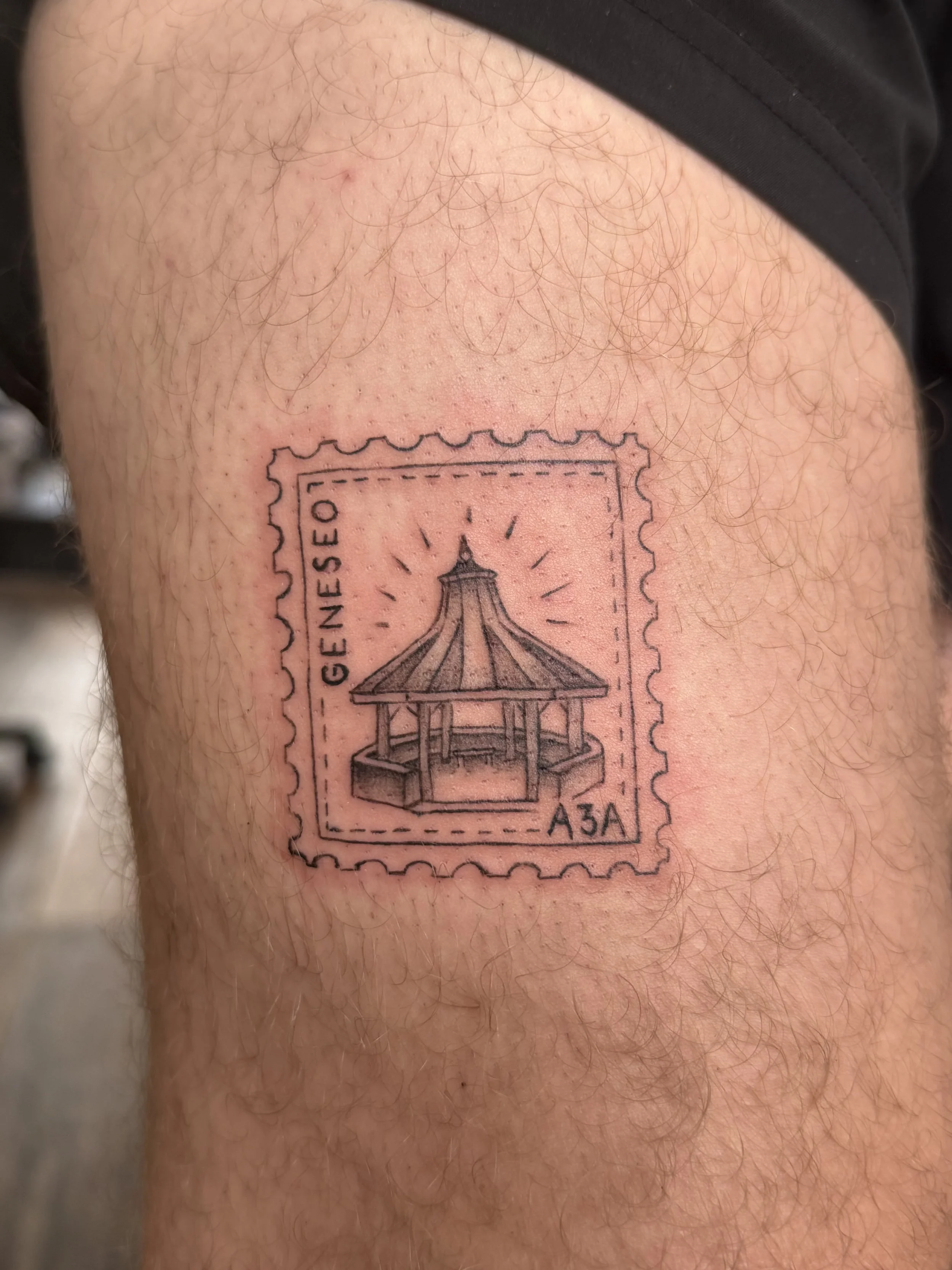Tattoo of a postage stamp featuring a pavilion with the words "Geneeseo" and the code "A34" on a person's leg with hair.