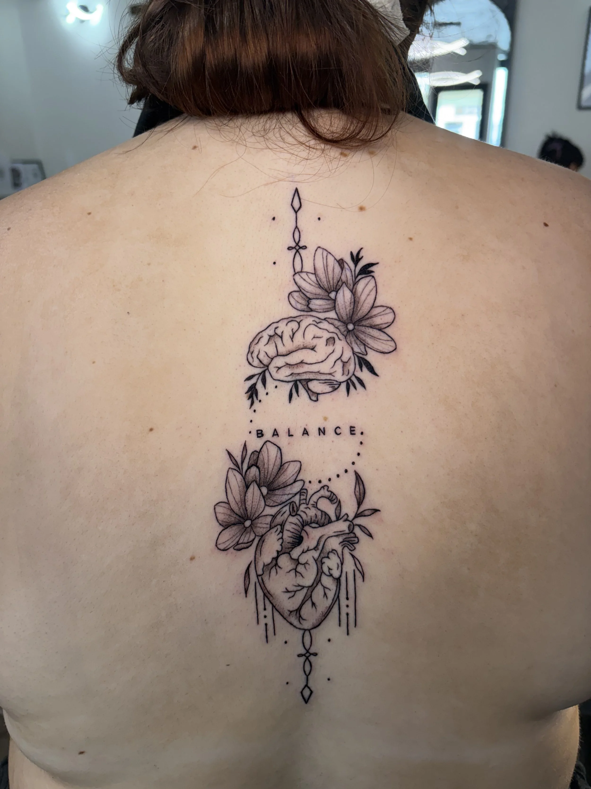 A tattoo on a person's upper chest featuring a detailed human heart surrounded by flowers and leaves, with the word 'BALANCE' written below.