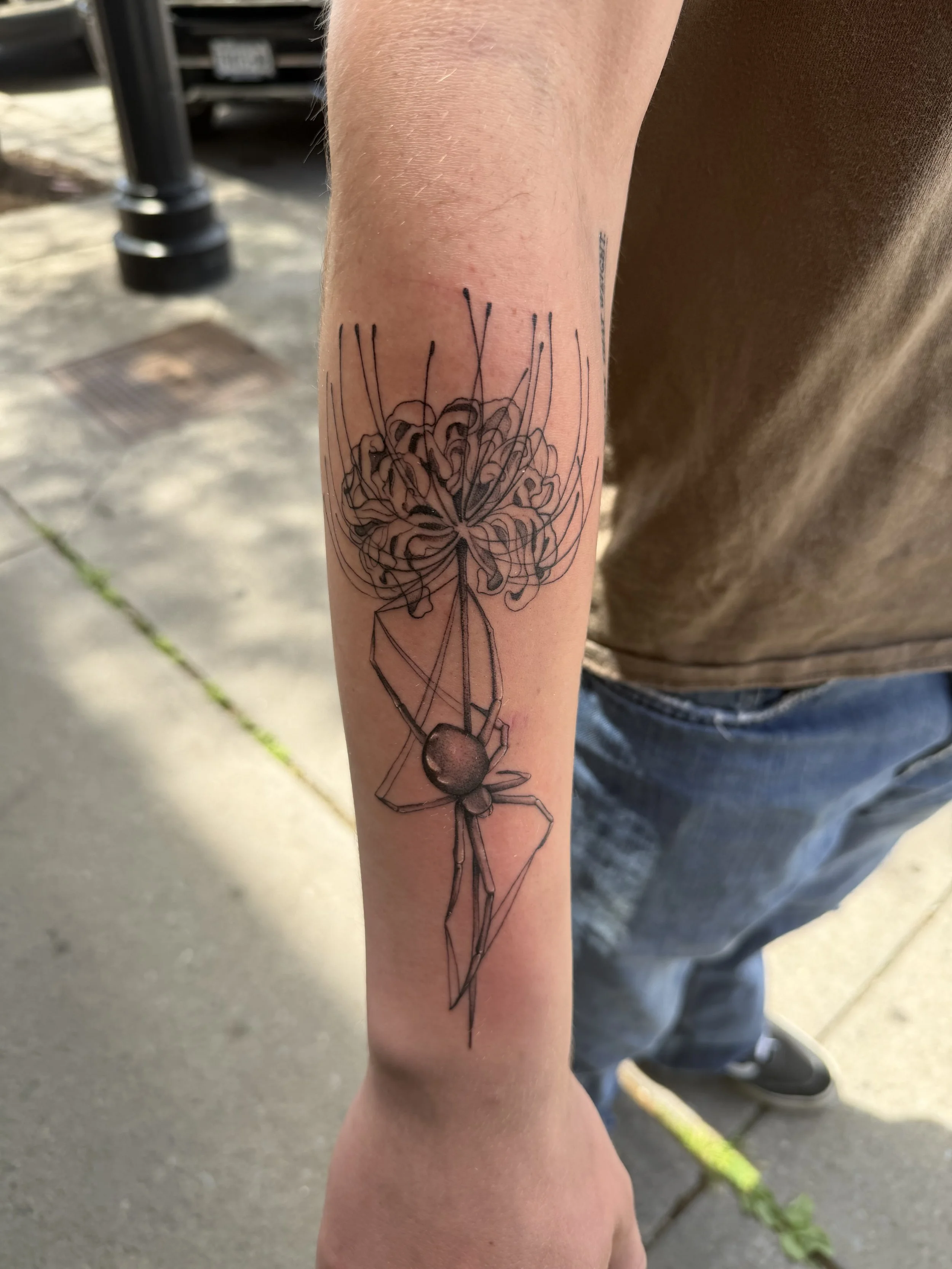A tattoo of a spider hanging from a web on a person's forearm.