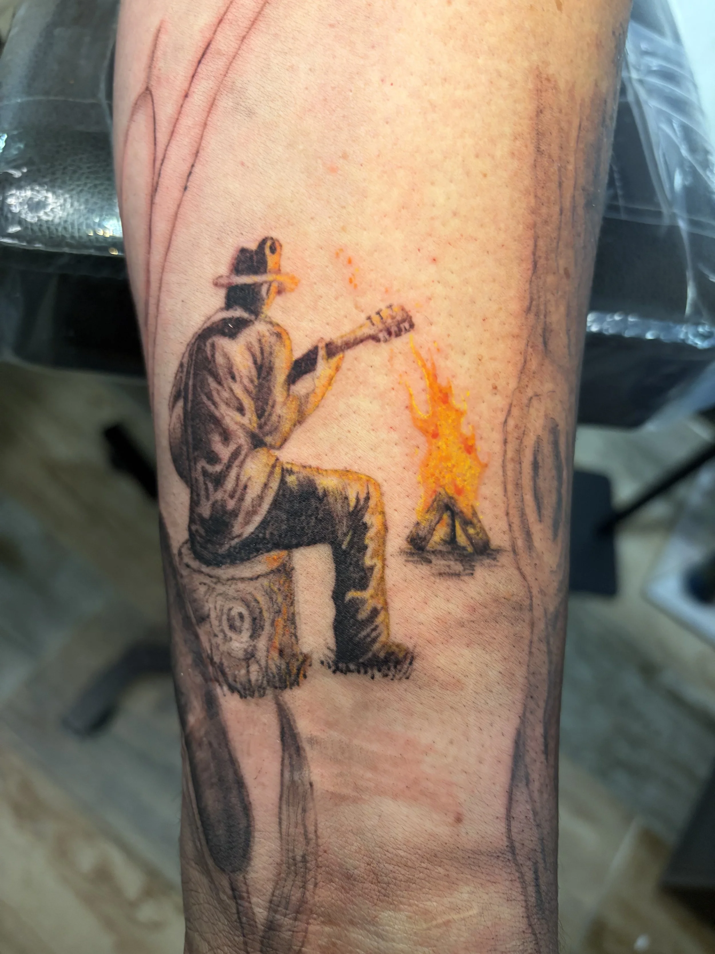 Tattoo of a man playing electric guitar, detailed in black and orange ink, on a person's arm.
