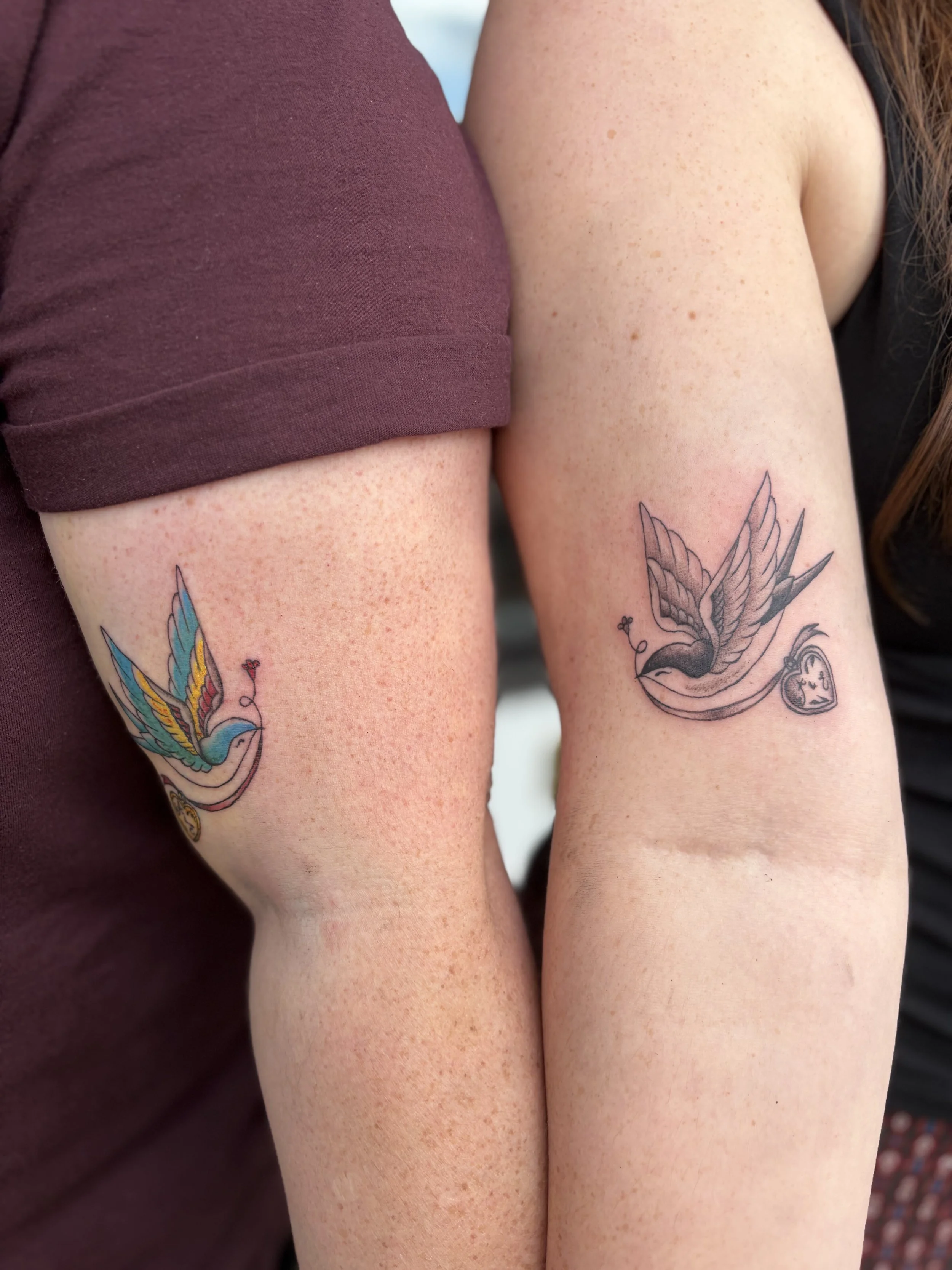Close-up of two arms with tattoos, one wearing a maroon sleeve, the other with natural skin tone, and a butterfly tattoo visible on one arm.
