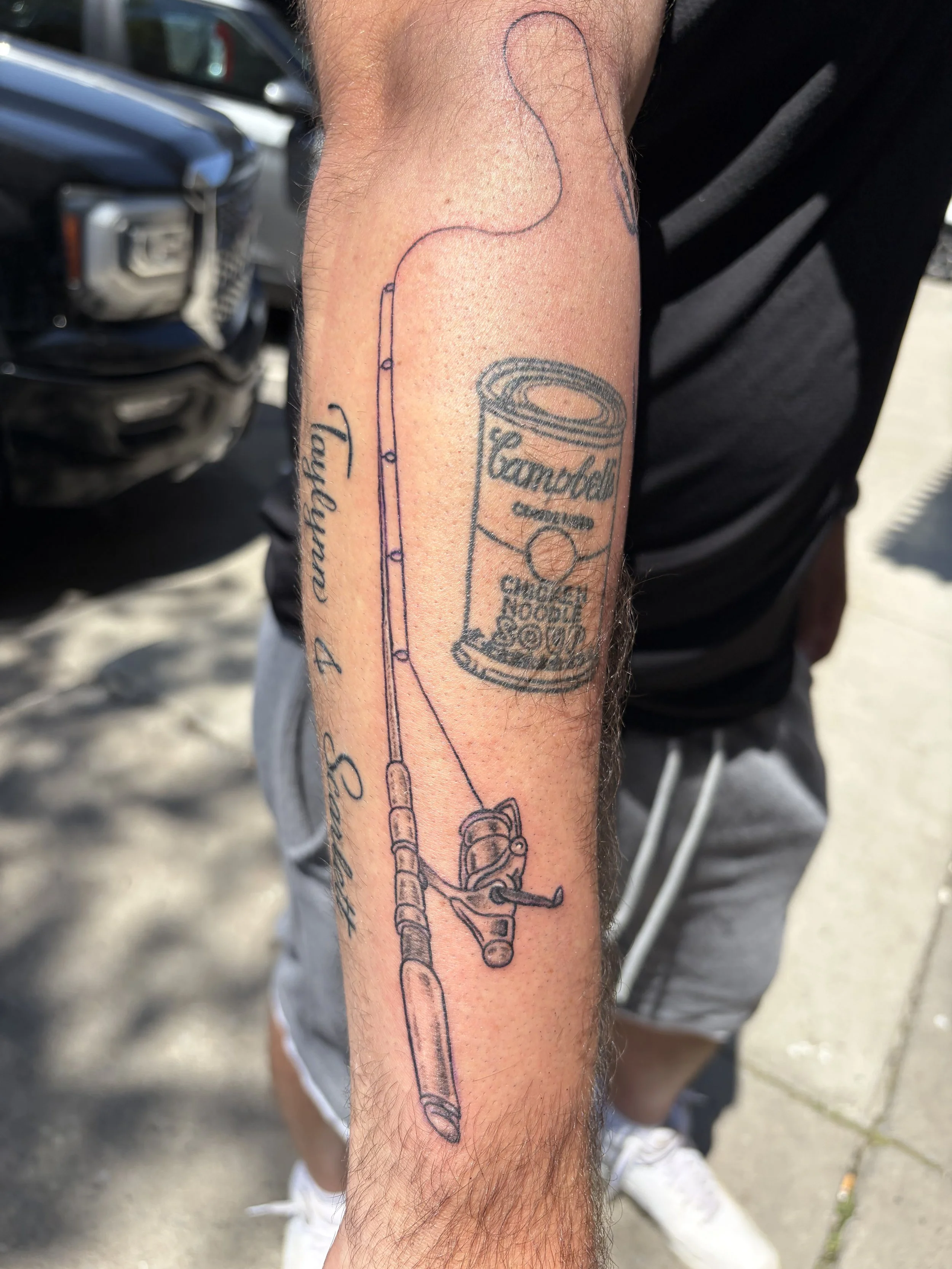 Tattoo of a fishing rod and a can of Campbell's Chunky Soup on a person's forearm.
