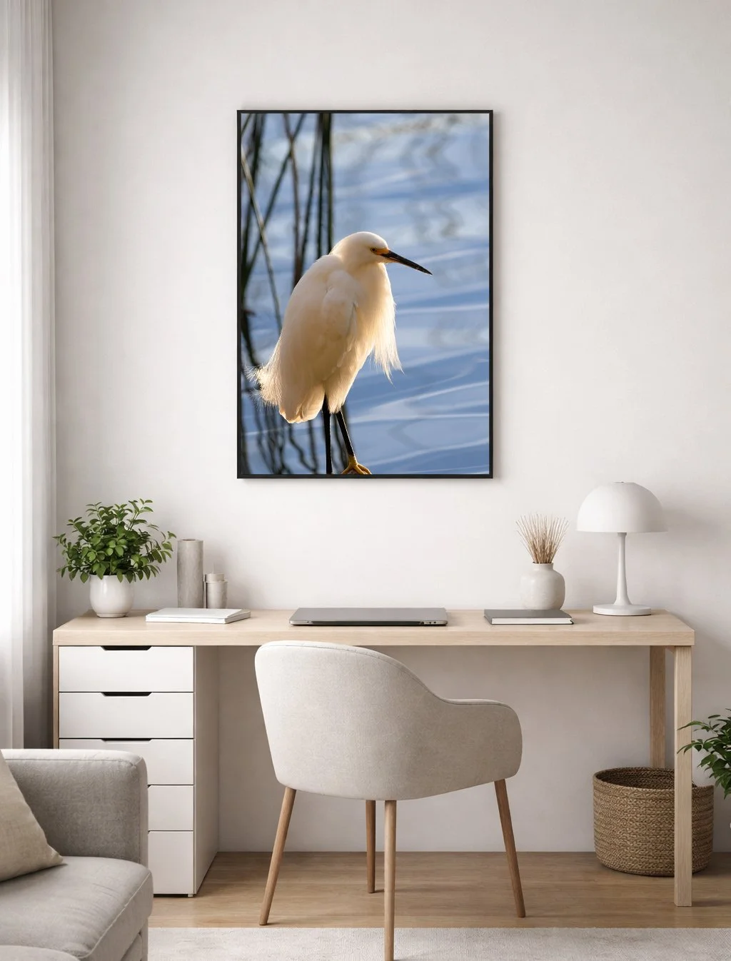 Decorative framed picture of a white heron on a wall above a desk in a modern, minimalist living space with a vase, books, and a plant.