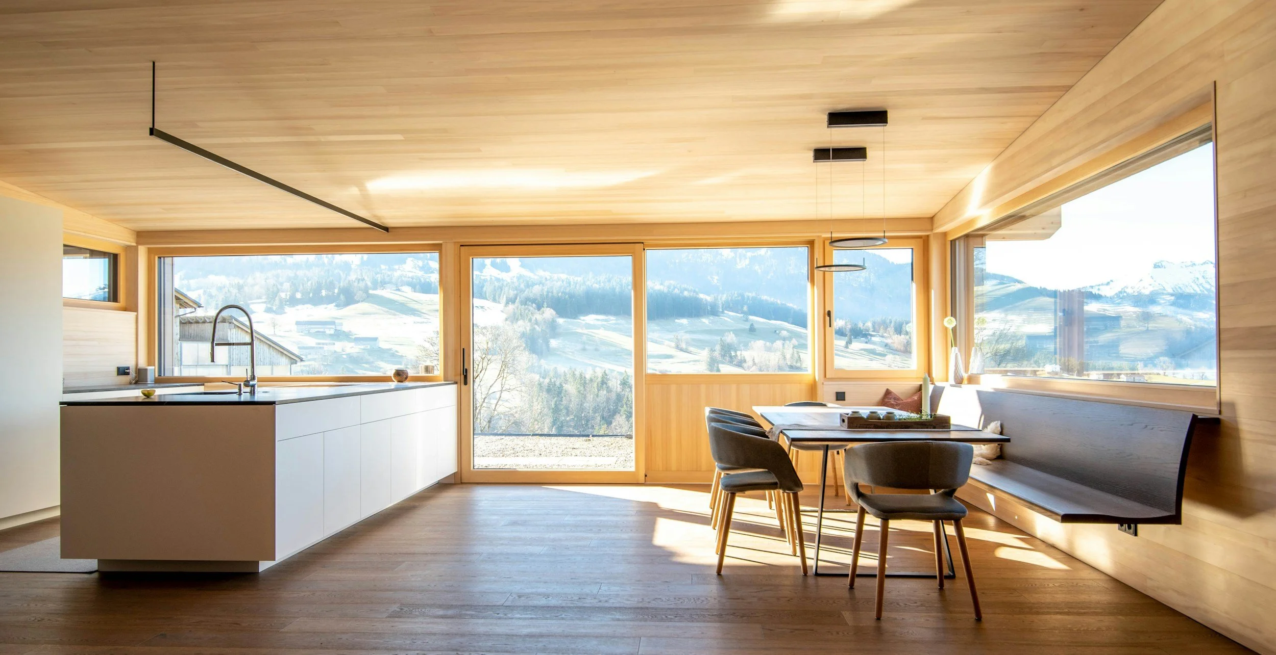 Modern kitchen and dining area with large windows showcasing a snowy mountain landscape.
