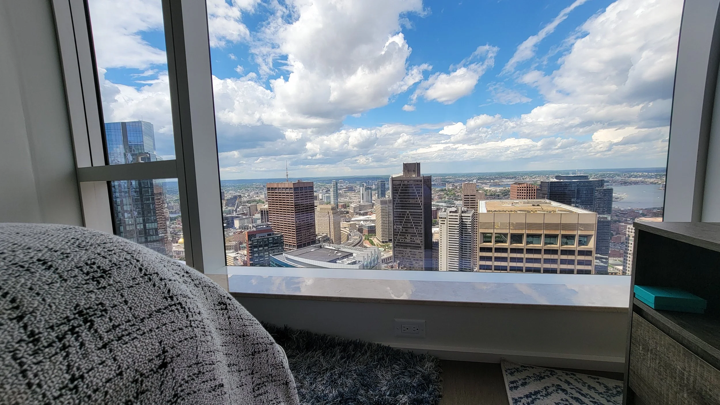 City skyline view from a high-rise apartment window with various skyscrapers and a river in the distance.