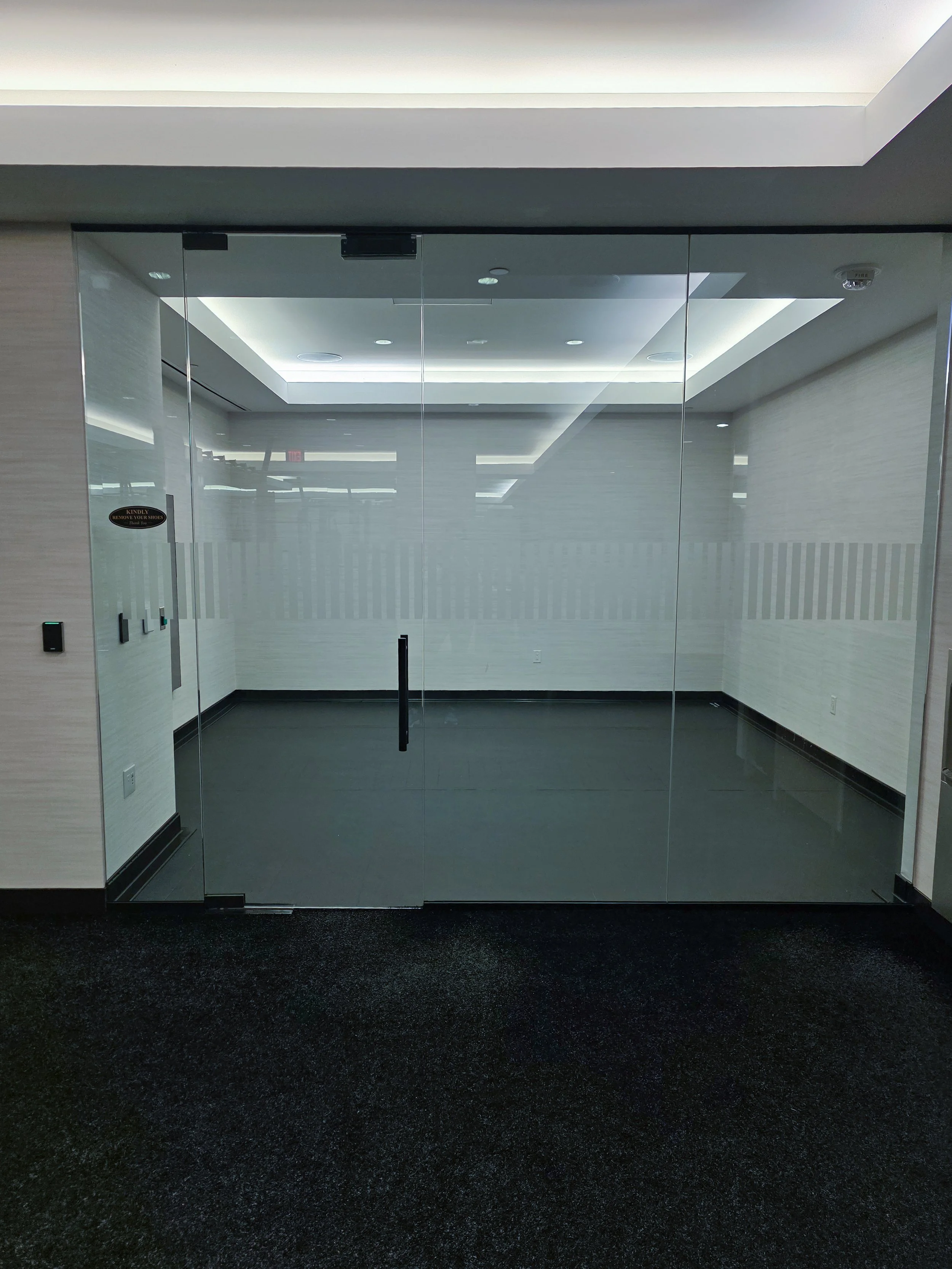 Empty glass entrance door in an office building with light-colored walls and dark flooring.