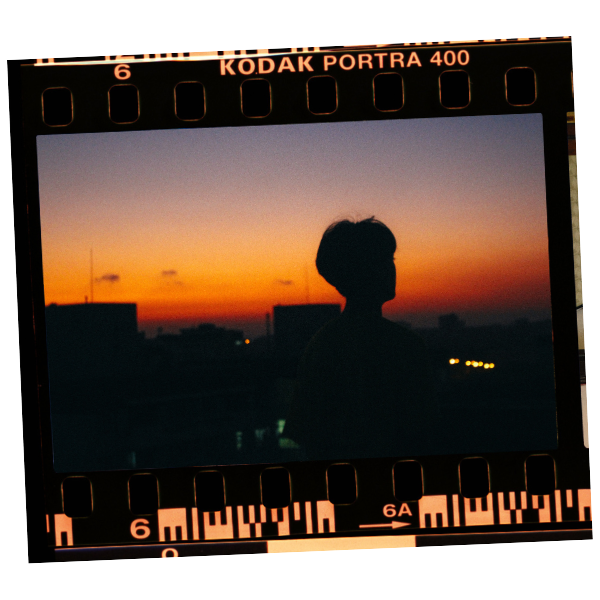 A person in silhouette standing outdoors at sunset, with a cityscape in the background. The photo is framed by Kodak Portra 400 film strip edges.