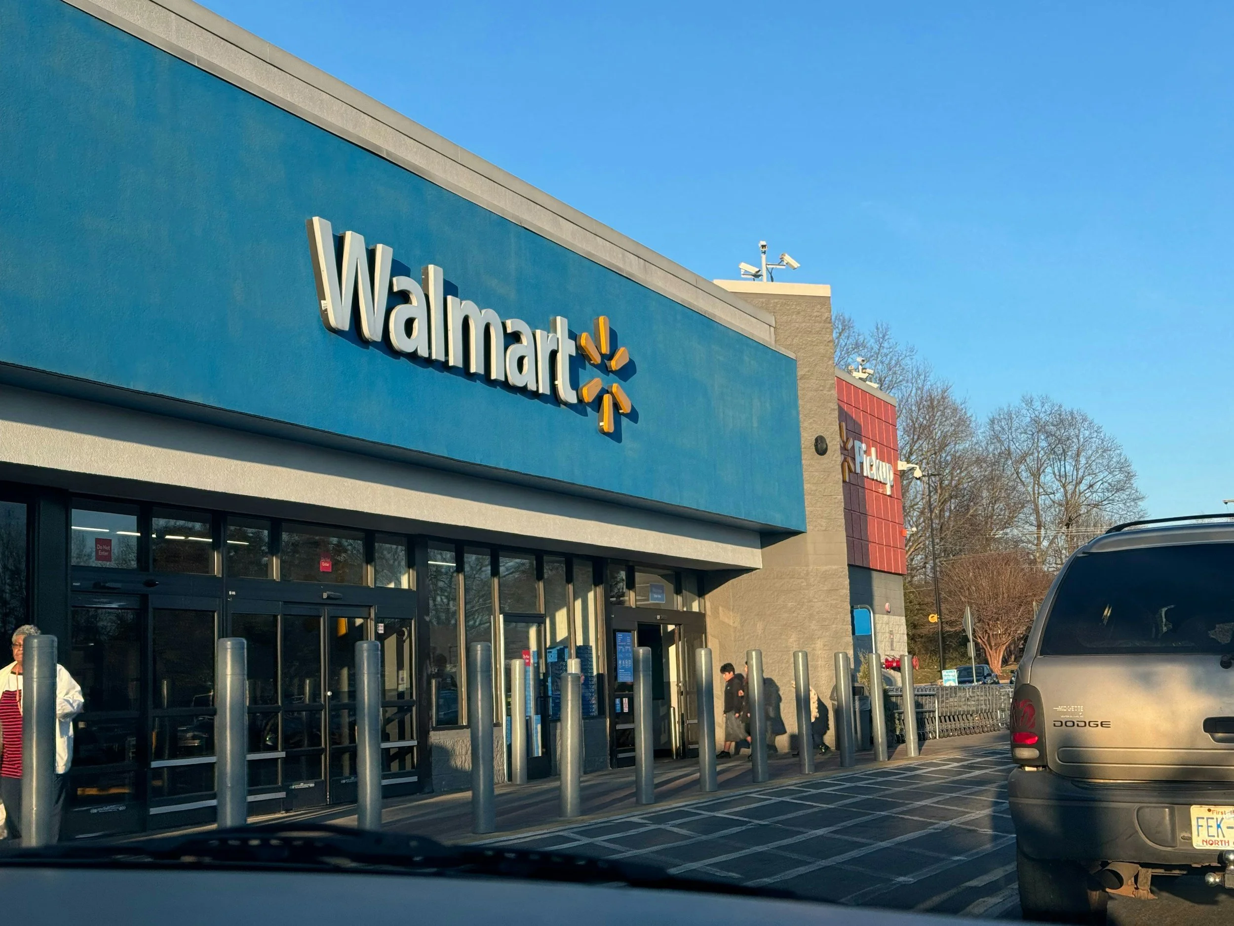View of a Walmart store entrance with several people and vehicles outside on a clear day.