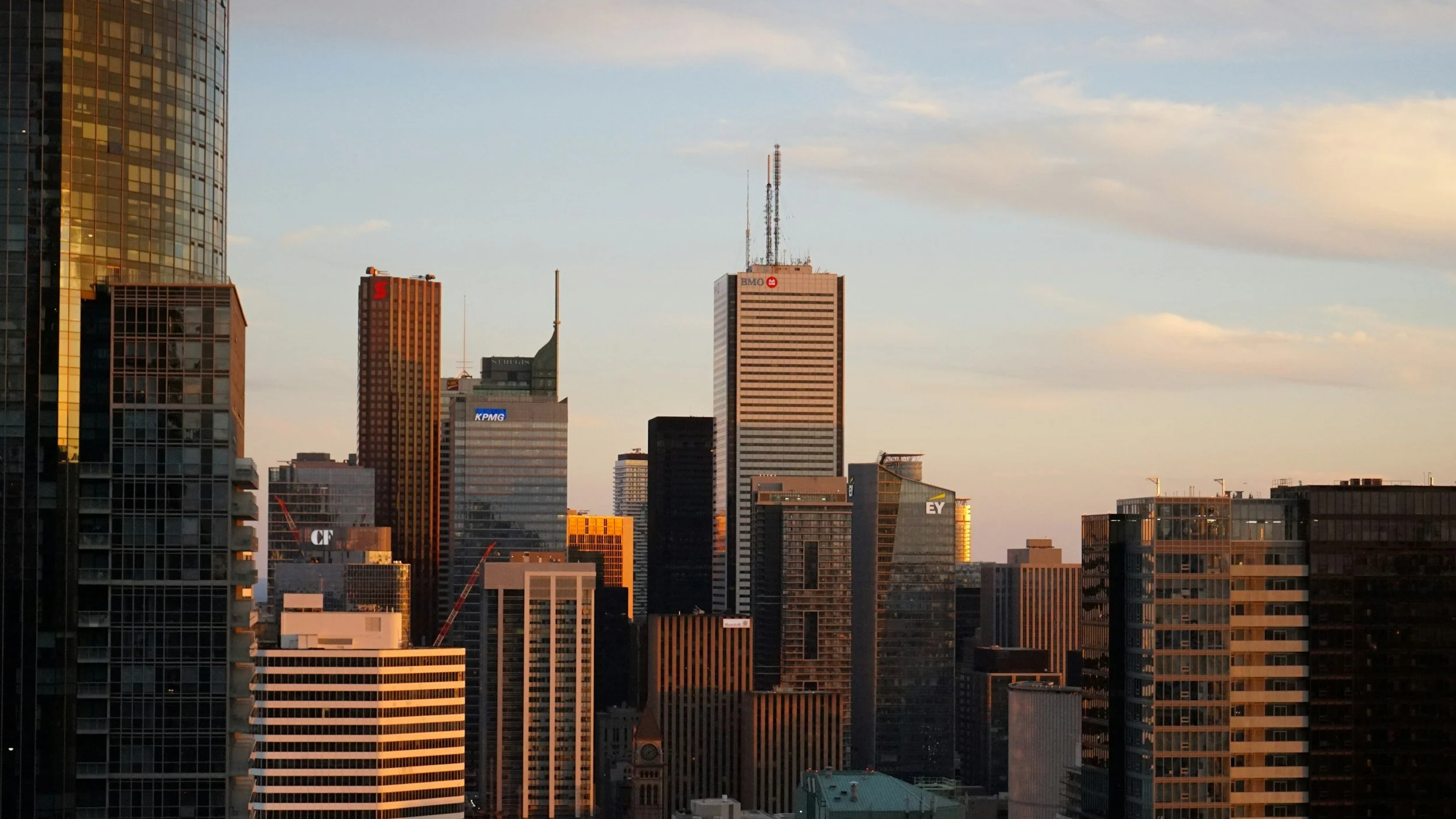 City skyline at sunset featuring high-rise buildings with illuminated windows, showcasing modern architecture with clear sky in the background.