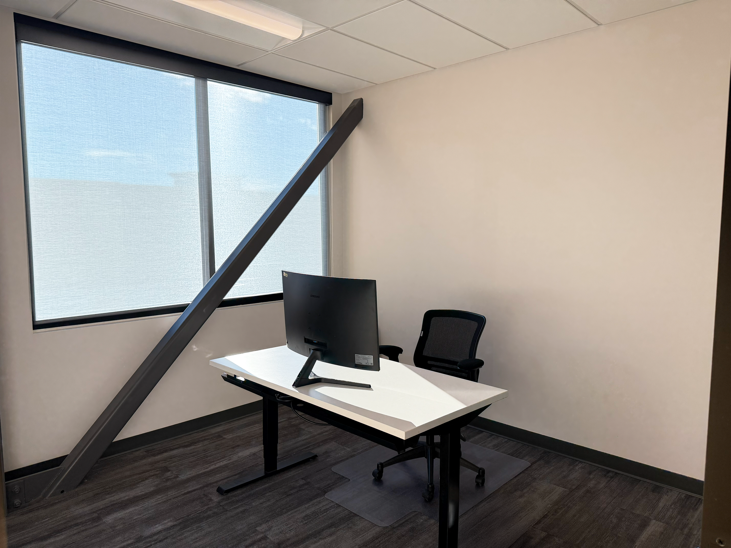 Move-in ready exterior office with a sit/stand desk, a computer monitor, an office chair, and a large window.