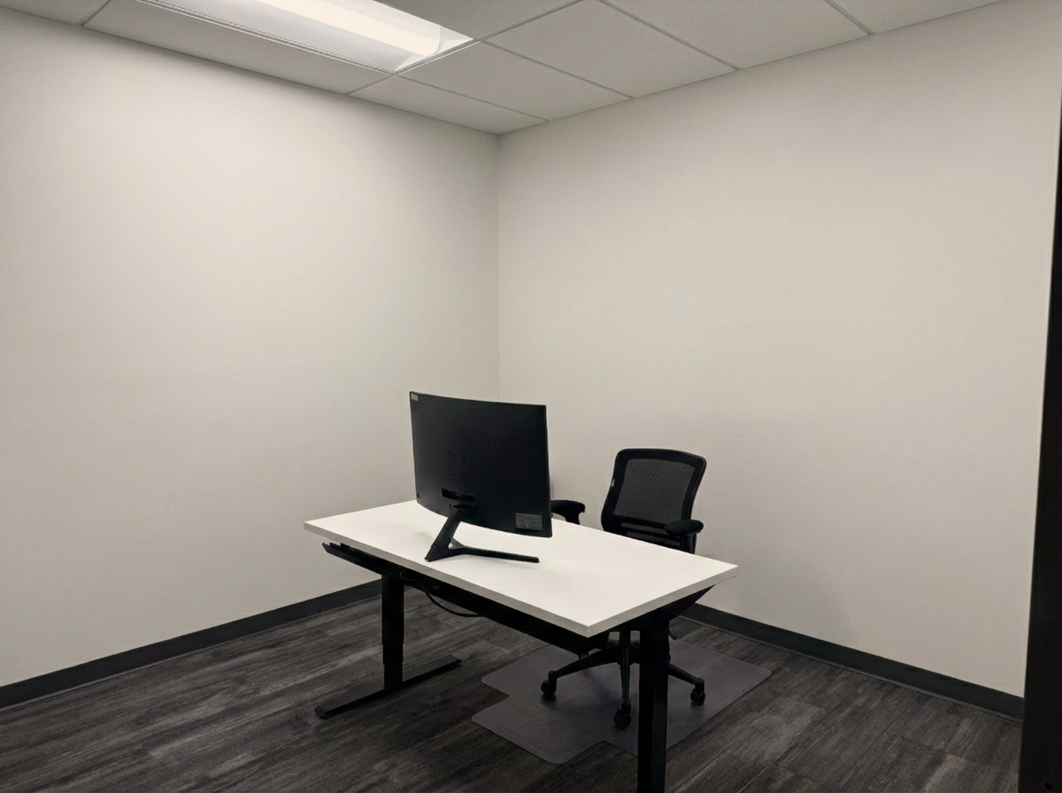 Interior office space with a sit/stand desk, a computer monitor, and an office chair. Move-in ready.
