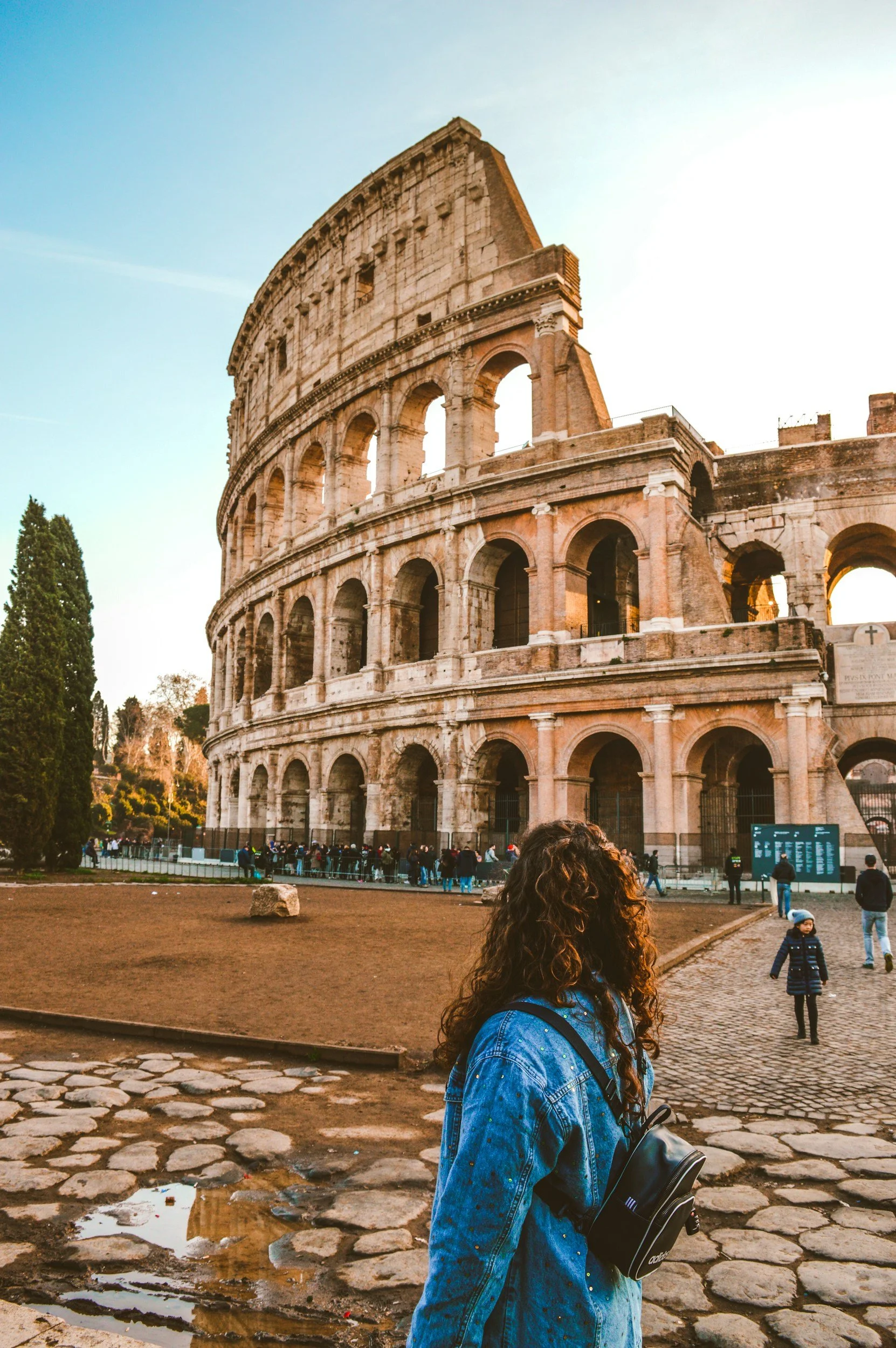 Tourist standing in front of the Colosseum in Rome, Italy, with a backpack, during sunset.