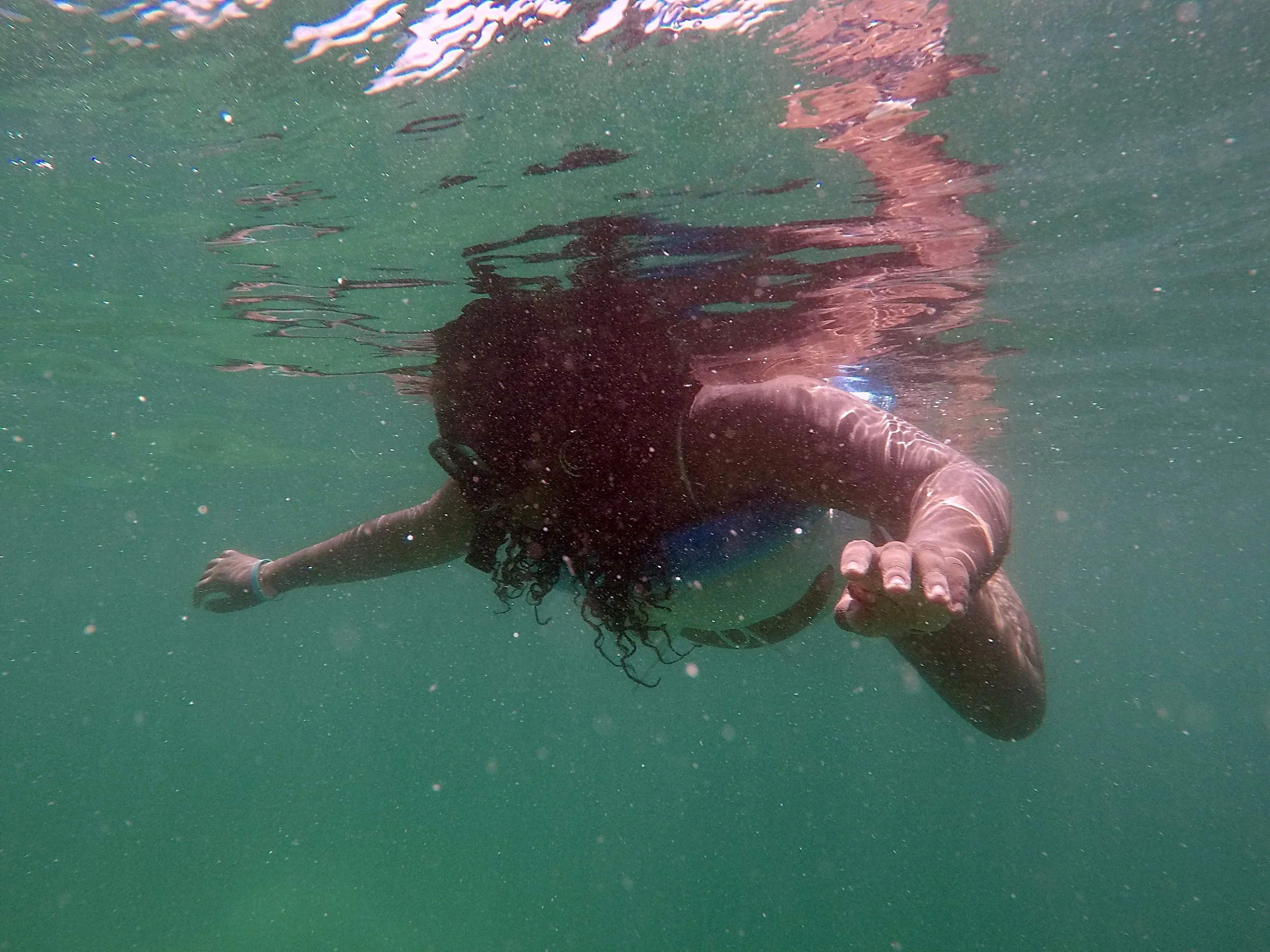 Person swimming underwater, reaching out with their hand towards the camera.