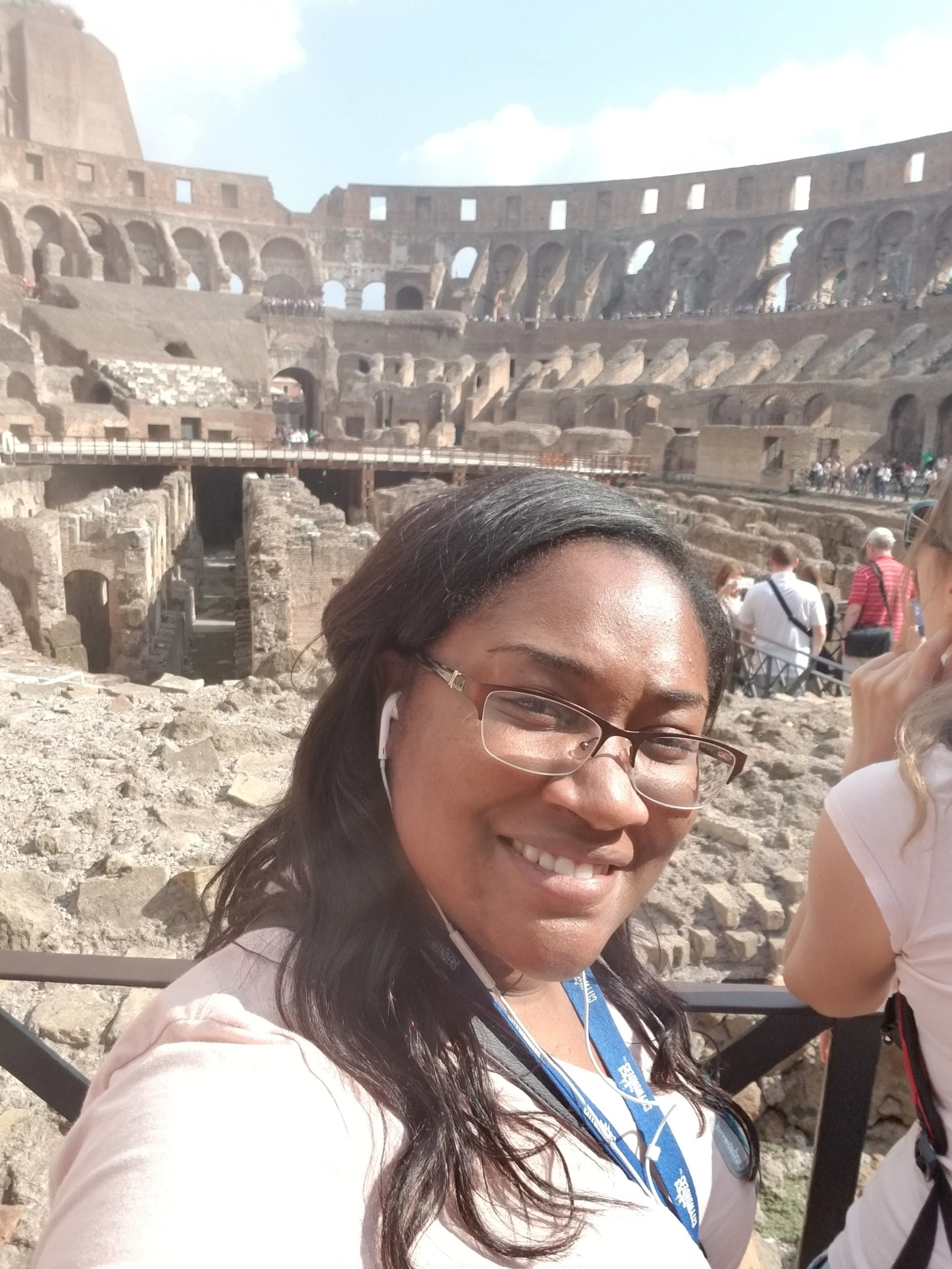 A woman smiling at the camera inside the Colosseum in Rome, Italy, with other tourists in the background.