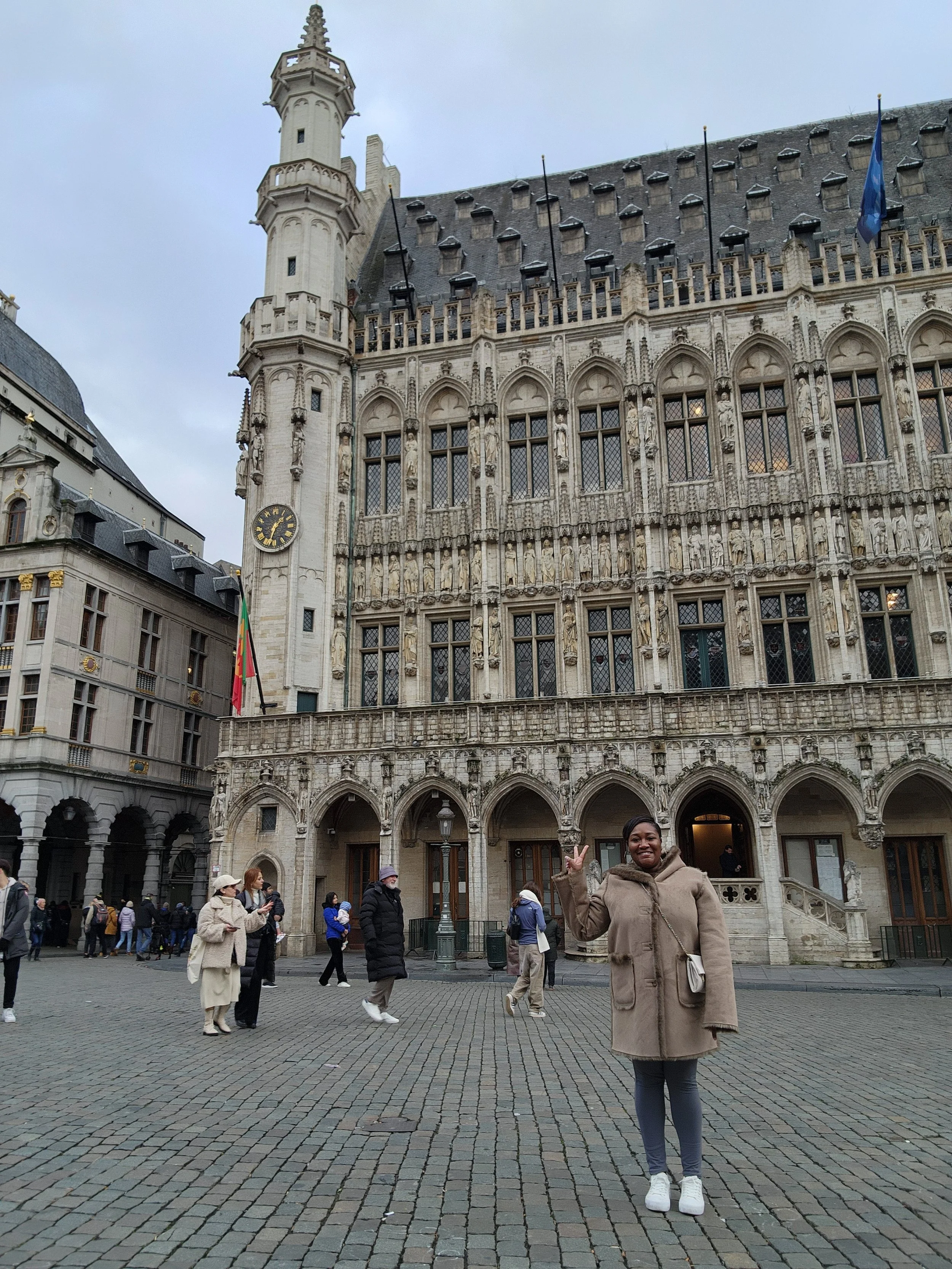 Woman posing in front of the Gothic-style city hall in Brussels, Belgium, with a crowd of tourists around.