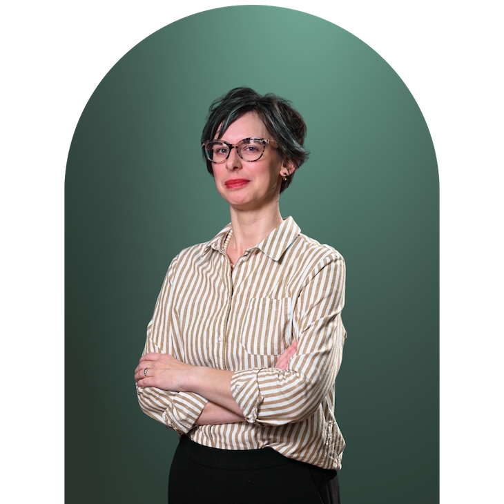 Barbara Isenberg, Fiscal New Yorker owner and financial coach. She has short dark hair and glasses wearing a beige and white striped blouse, standing with arms crossed against a green background.