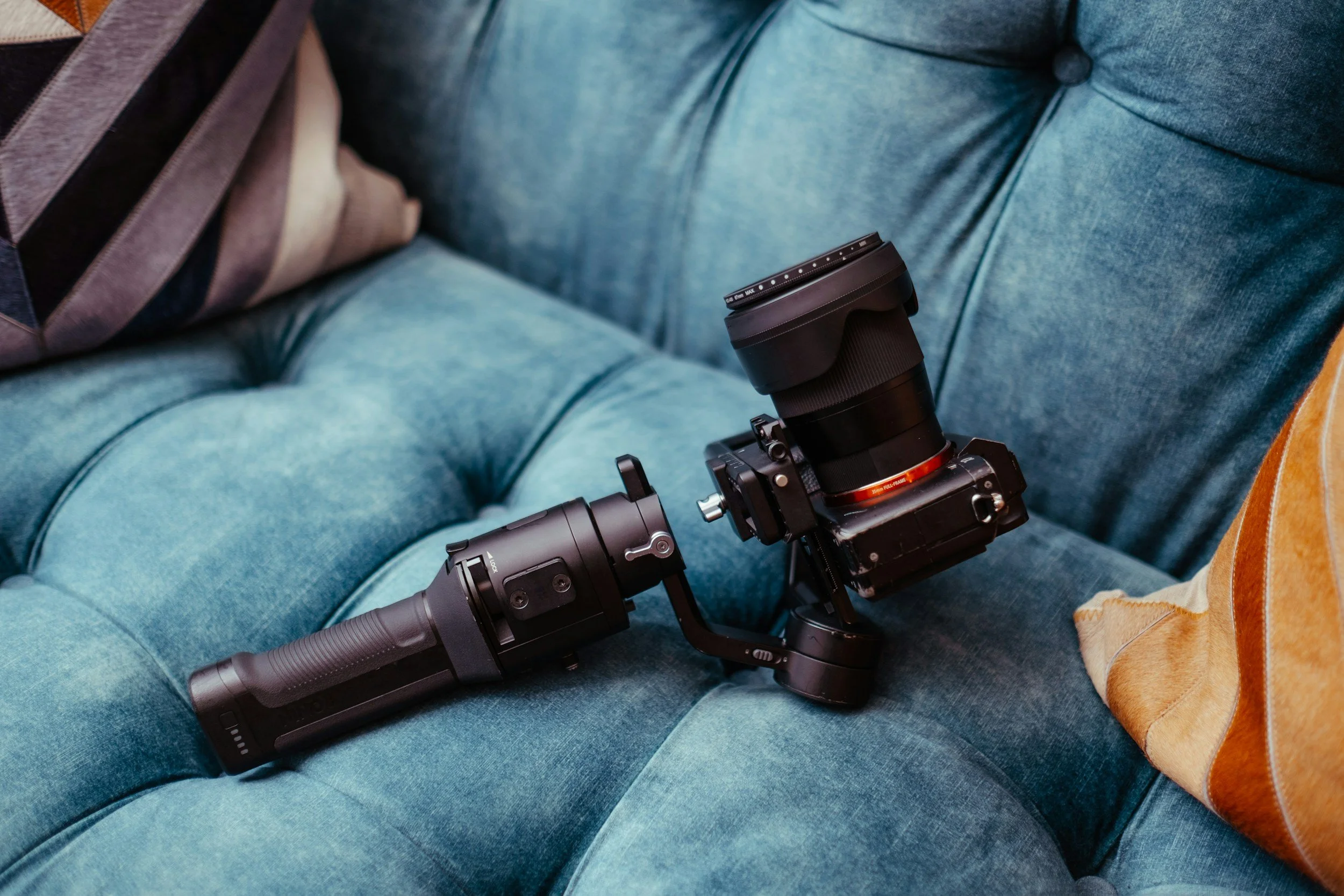Camera stabilizer with camera mounted, placed on a teal tufted sofa.