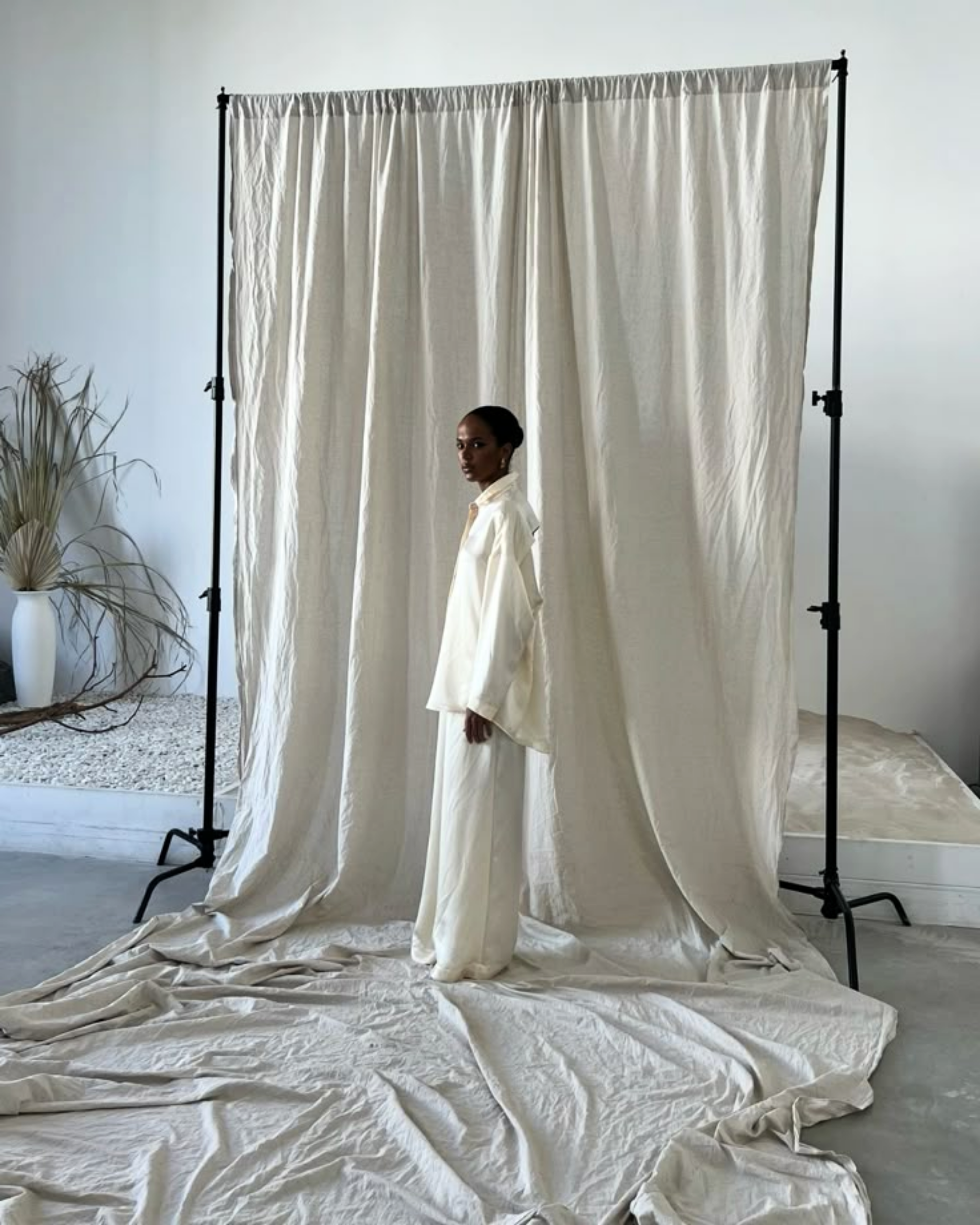 A woman in an all-white outfit standing inside a beige curtain backdrop in a studio.