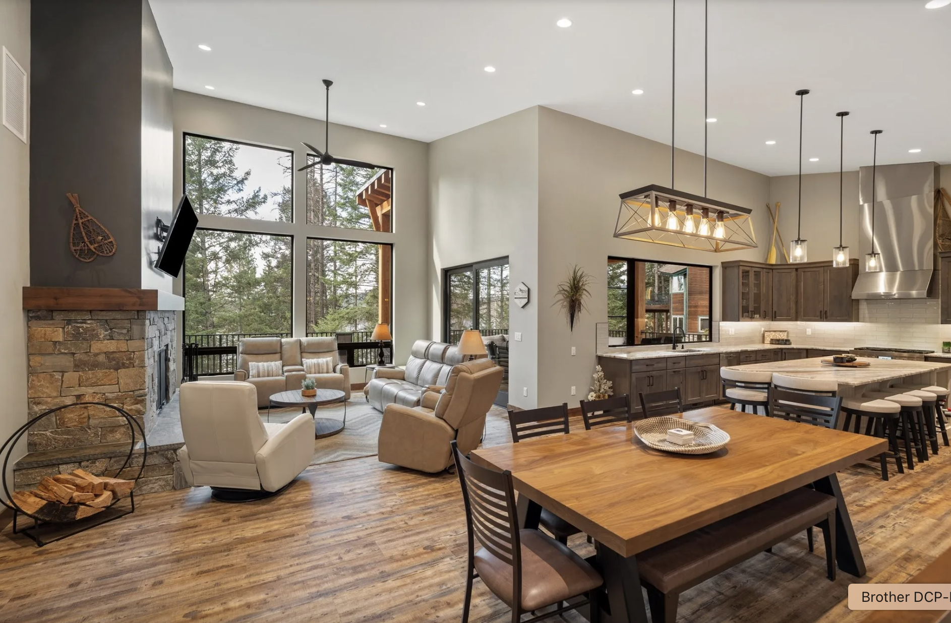 Open-concept living room and kitchen with large windows, wooden flooring, modern furniture, and a wood-burning fireplace.