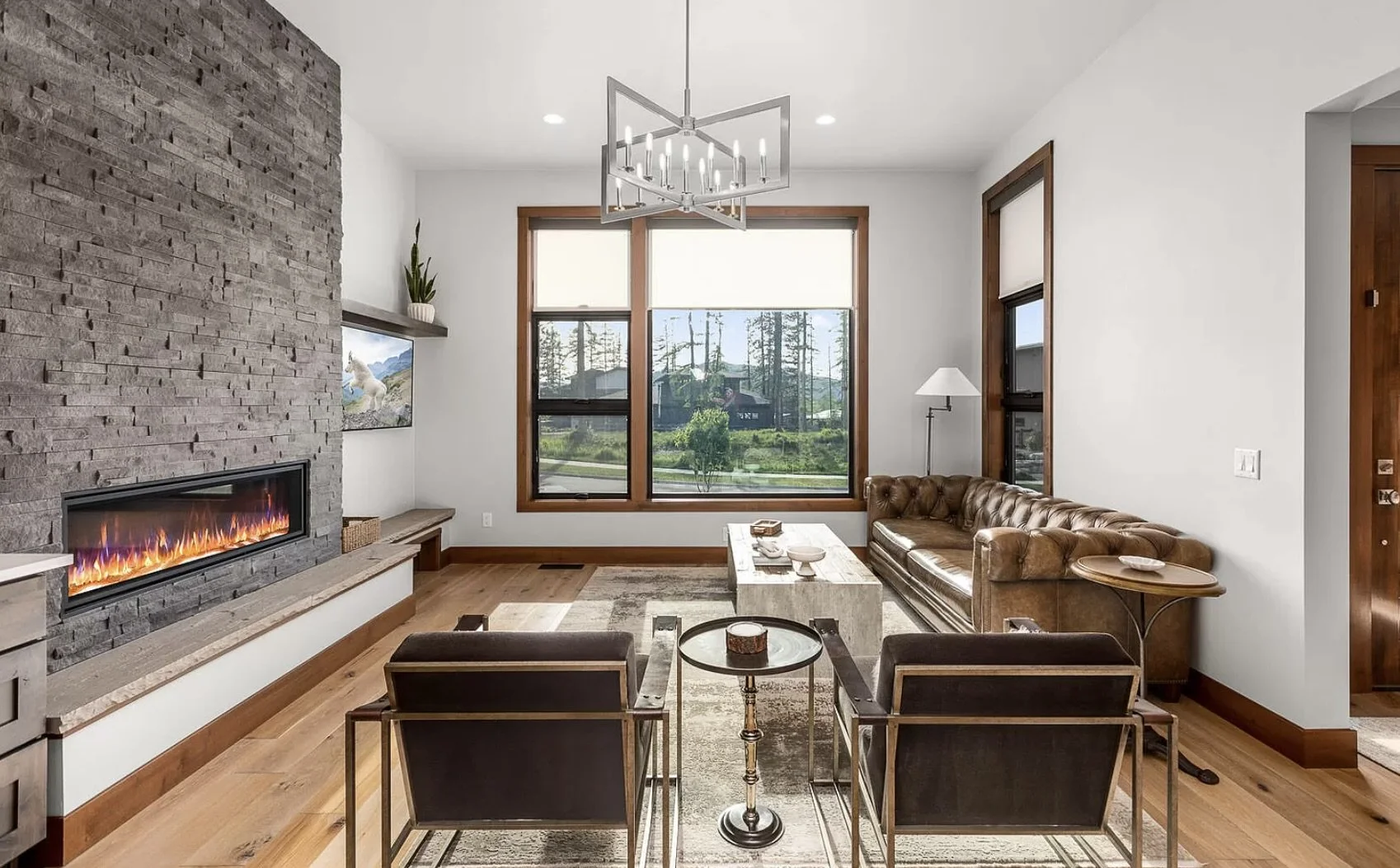 Modern living room with large window, leather sofa, armchairs, fireplace, and minimal decor.