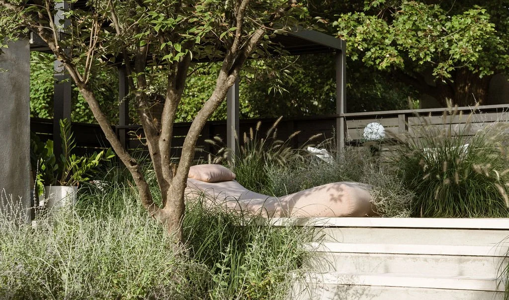 Outdoor lounge chair with pillow on a set of steps surrounded by greenery and plants.