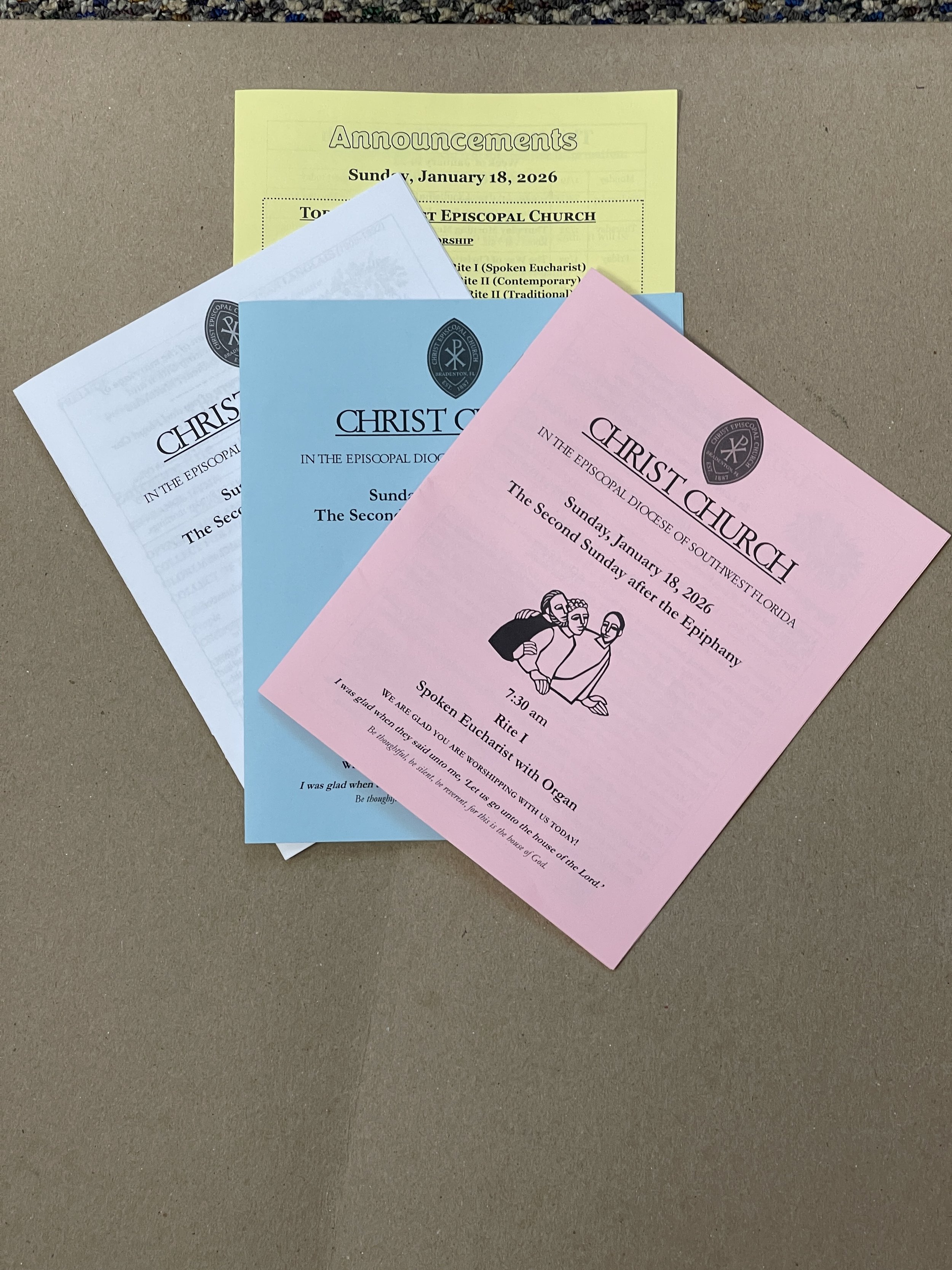 A collection of church bulletins and announcements from Christ Church in South Florida, displayed on a beige surface. The bulletins are in different colors: yellow, blue, and pink.