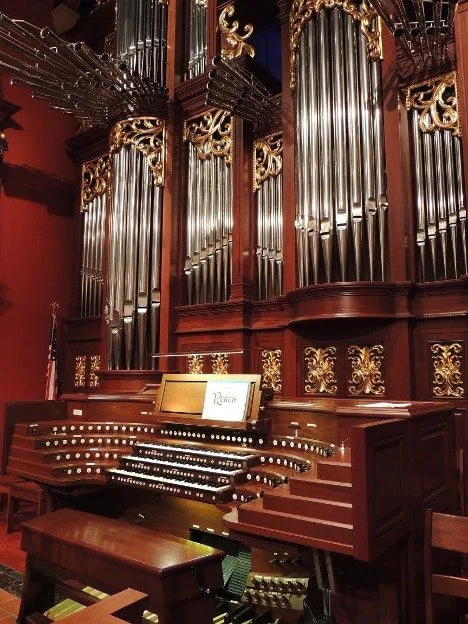 A pipe organ with large metal pipes, wood paneling, and gold decorative accents inside a church or concert hall.