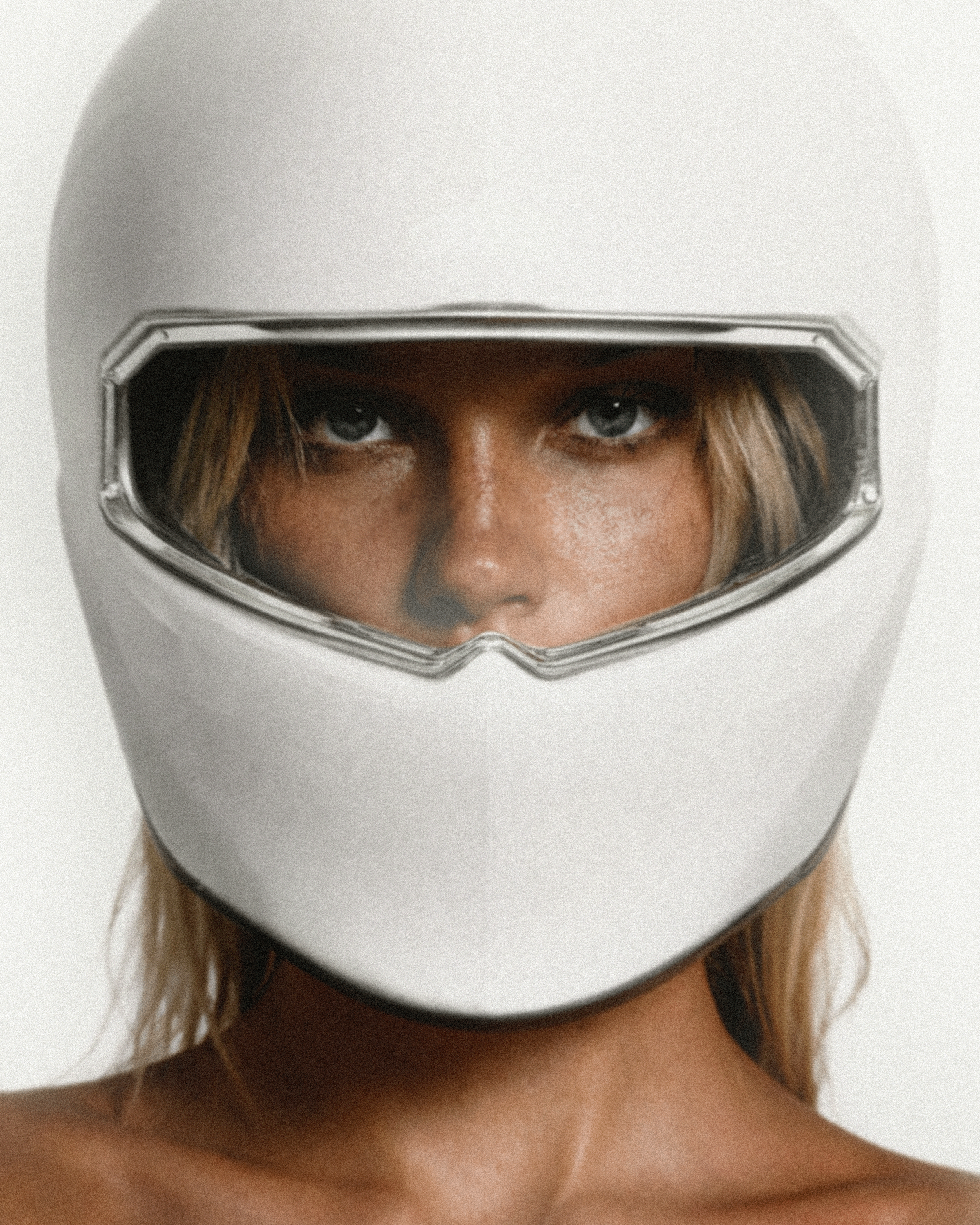 A woman with light skin and blue eyes wearing a white motorcycle helmet with a clear visor, showing her face and eyes.