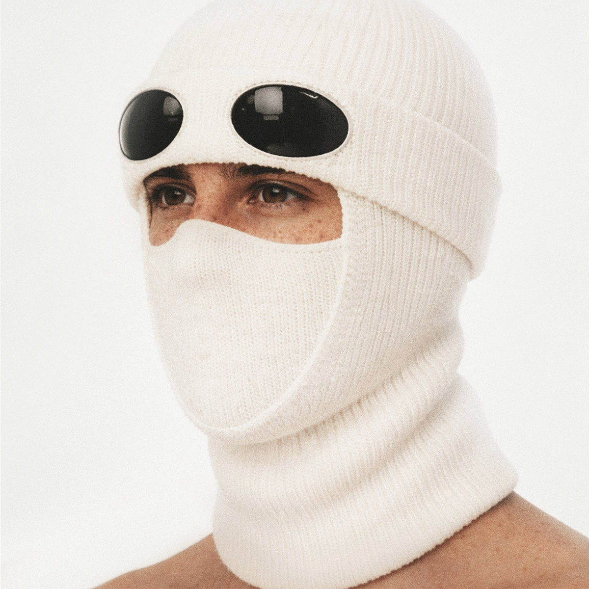 Person wearing a white balaclava with large black goggles on forehead, looking to the side.
