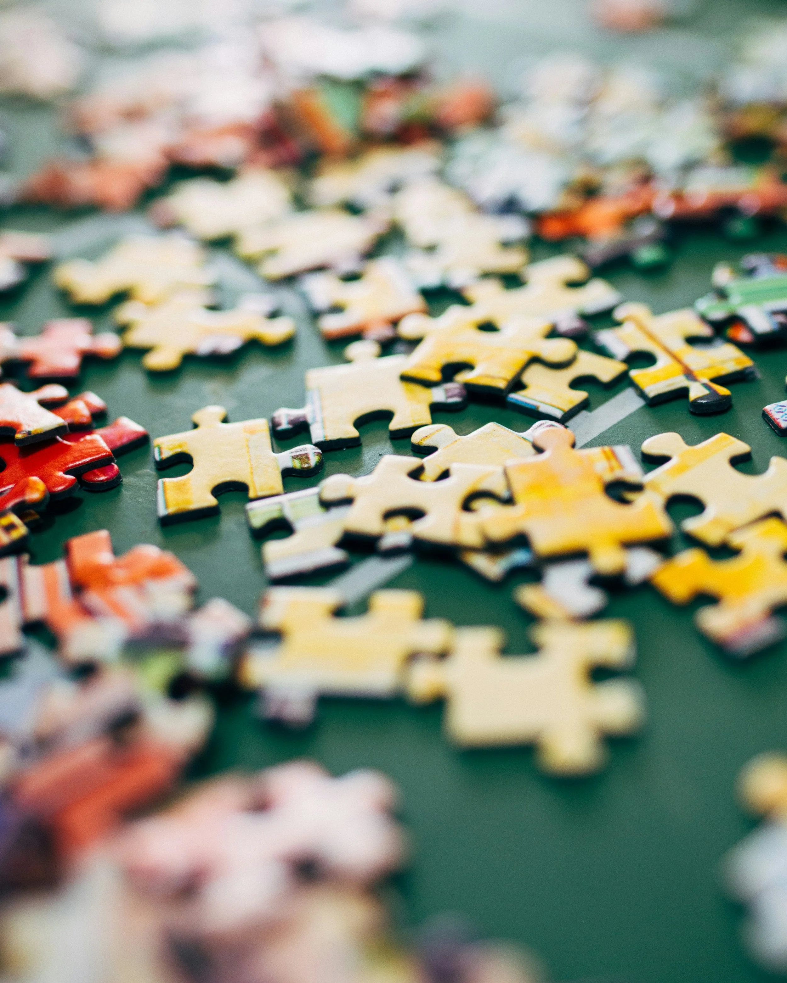 Close-up of scattered puzzle pieces on a green surface, with some pieces showing colorful patterns.