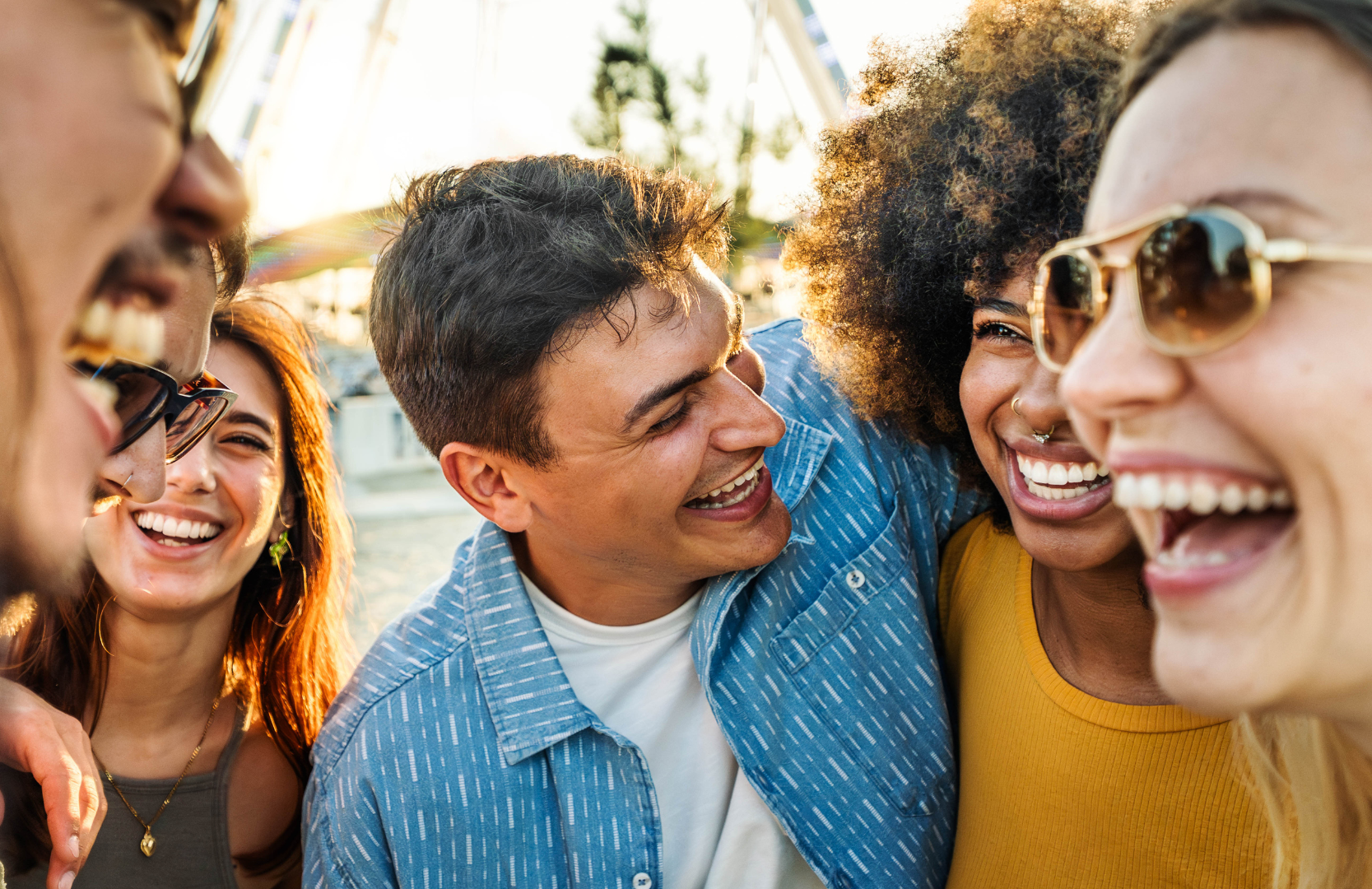 A group of friends smiling and laughing close together outdoors during sunset.