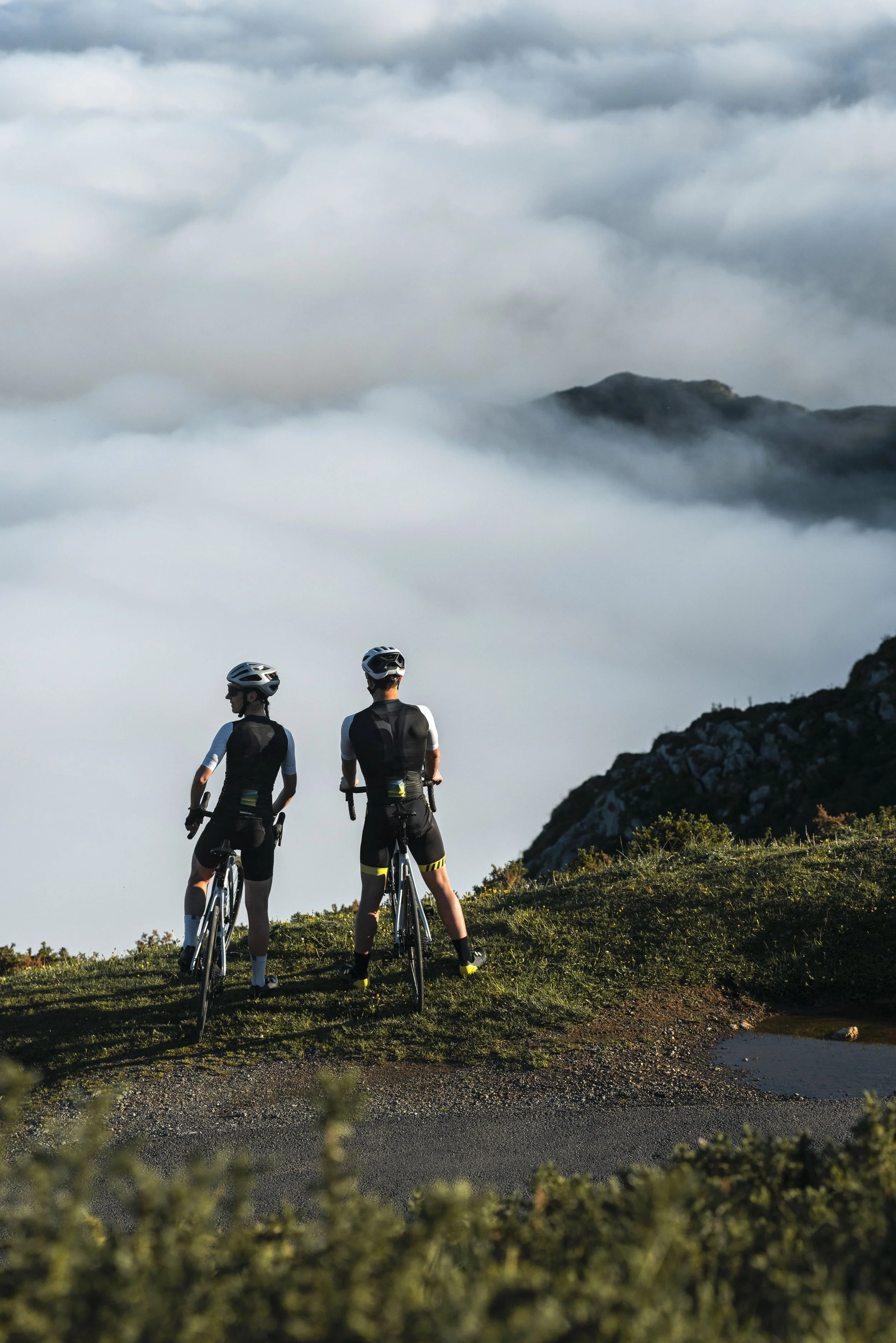 Amigos treinando juntos de bicicleta em uma estrada rural cercada por montanhas cobertas de neblina durante o verão