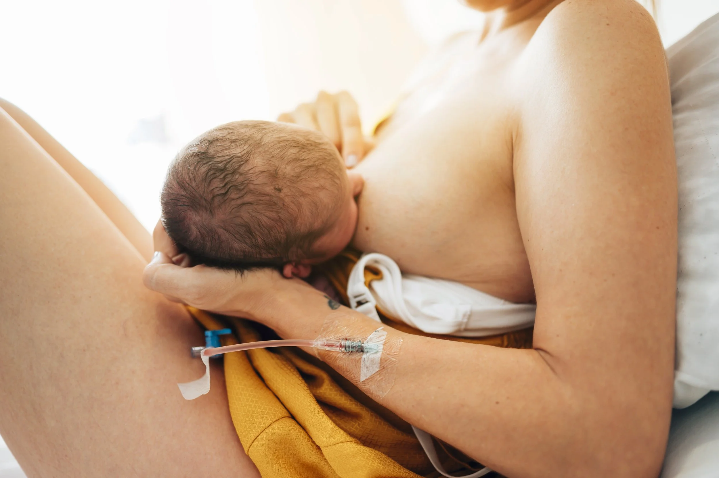 A mother breastfeeding her newborn in a hospital bed with medical equipment nearby.