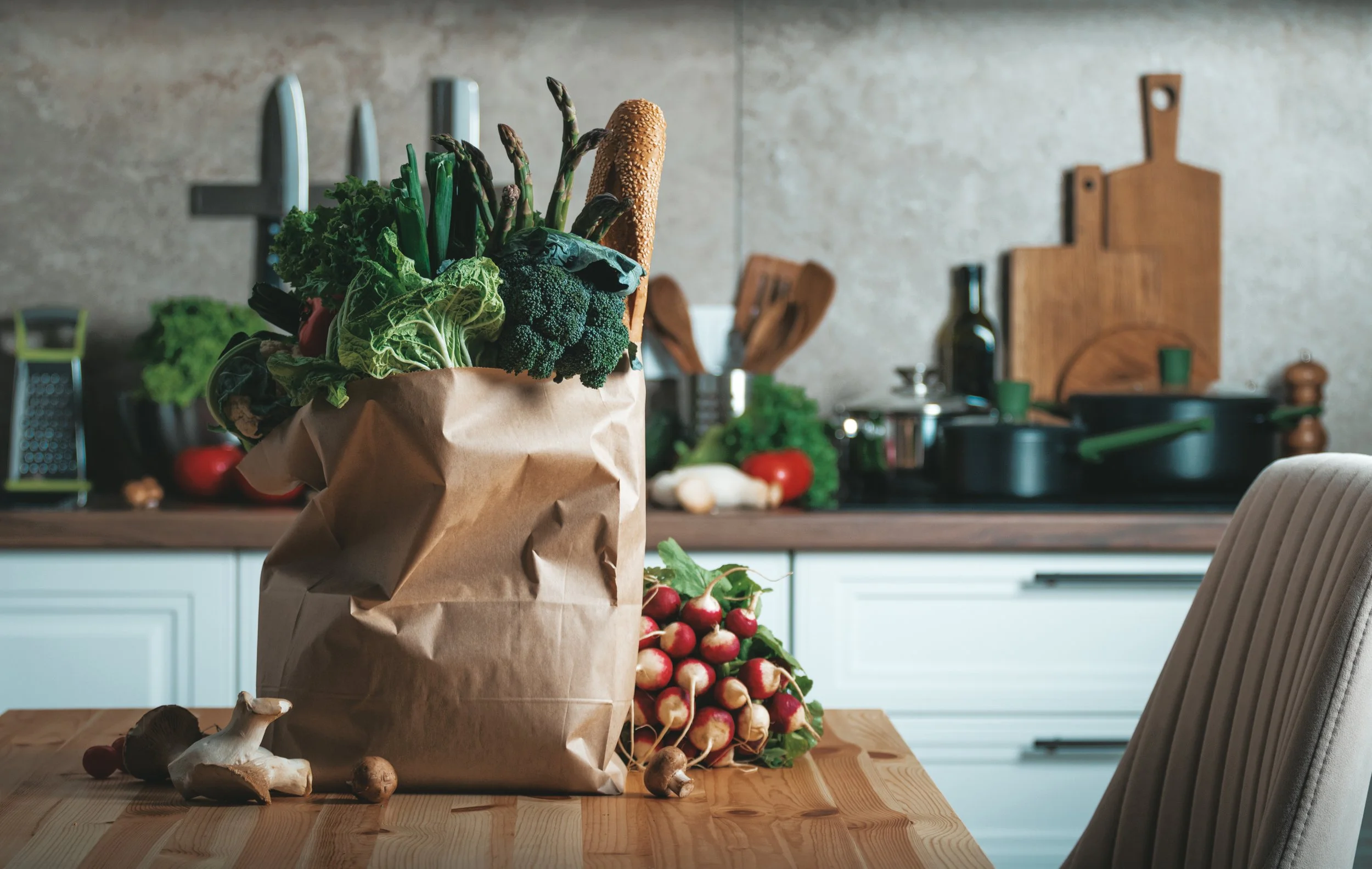 Fresh vegetables overflowing from a paper grocery bag on a kitchen counter