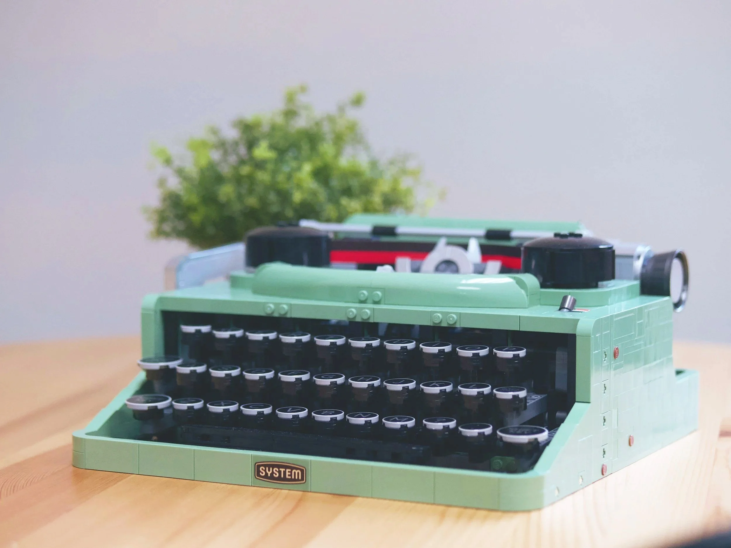 Lego-Rechenmaschine aus grünen und schwarzen Legosteinen mit einem Baum im Hintergrund auf einem Holztisch.