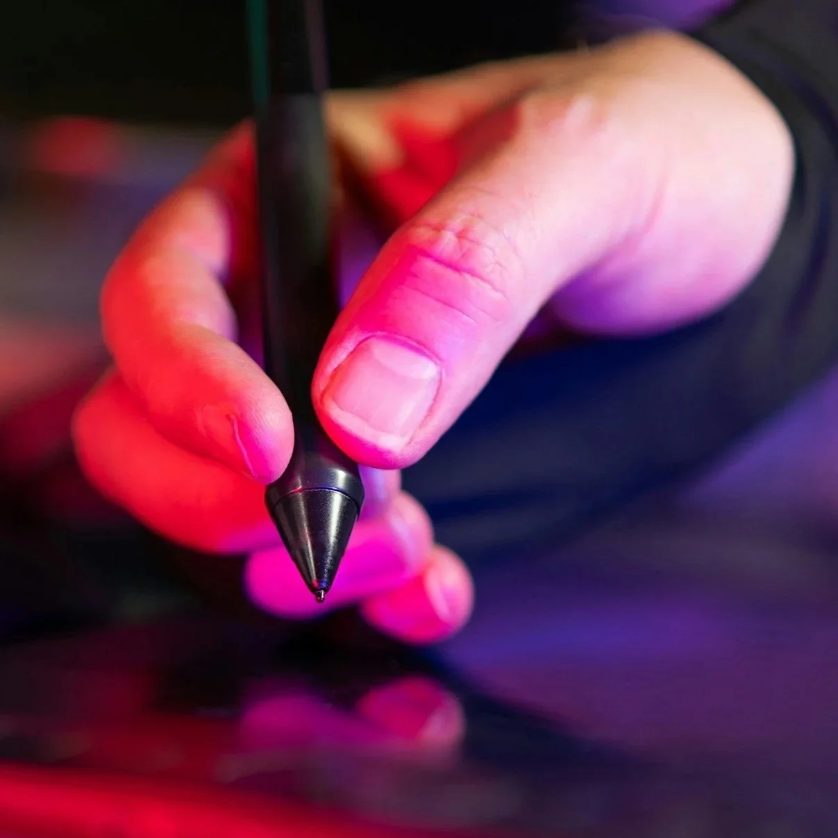 Nahaufnahme einer Hand, die mit einem digitalen Stift auf einer Oberfläche schreibt, beleuchtet von farbigem Licht beim skizzieren eines Designs.