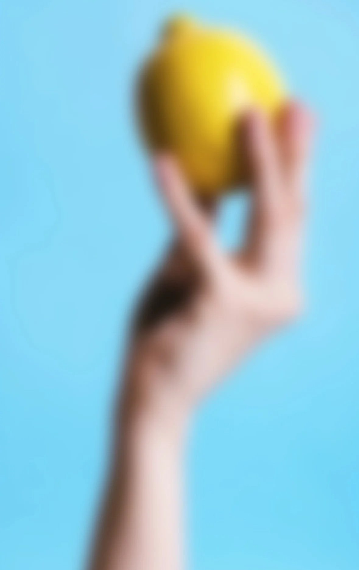 Ein unscharfes Bild einer Hand, die eine gelbe Zitrone gegen einen hellblauen Hintergrund hält.