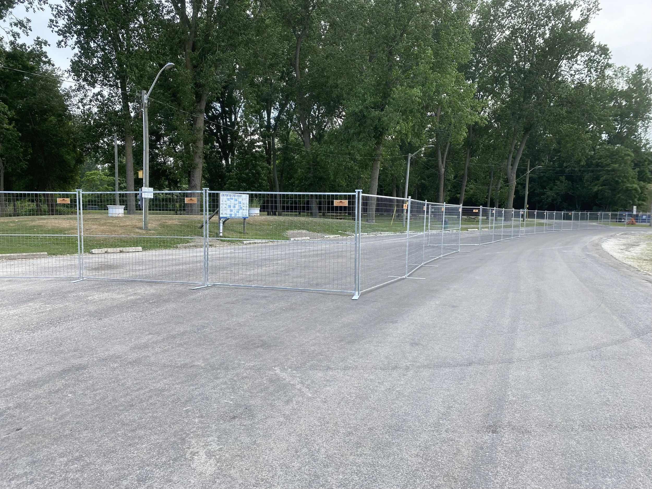 Fenced-off area on a paved road with trees in the background, streetlights, and a sign.