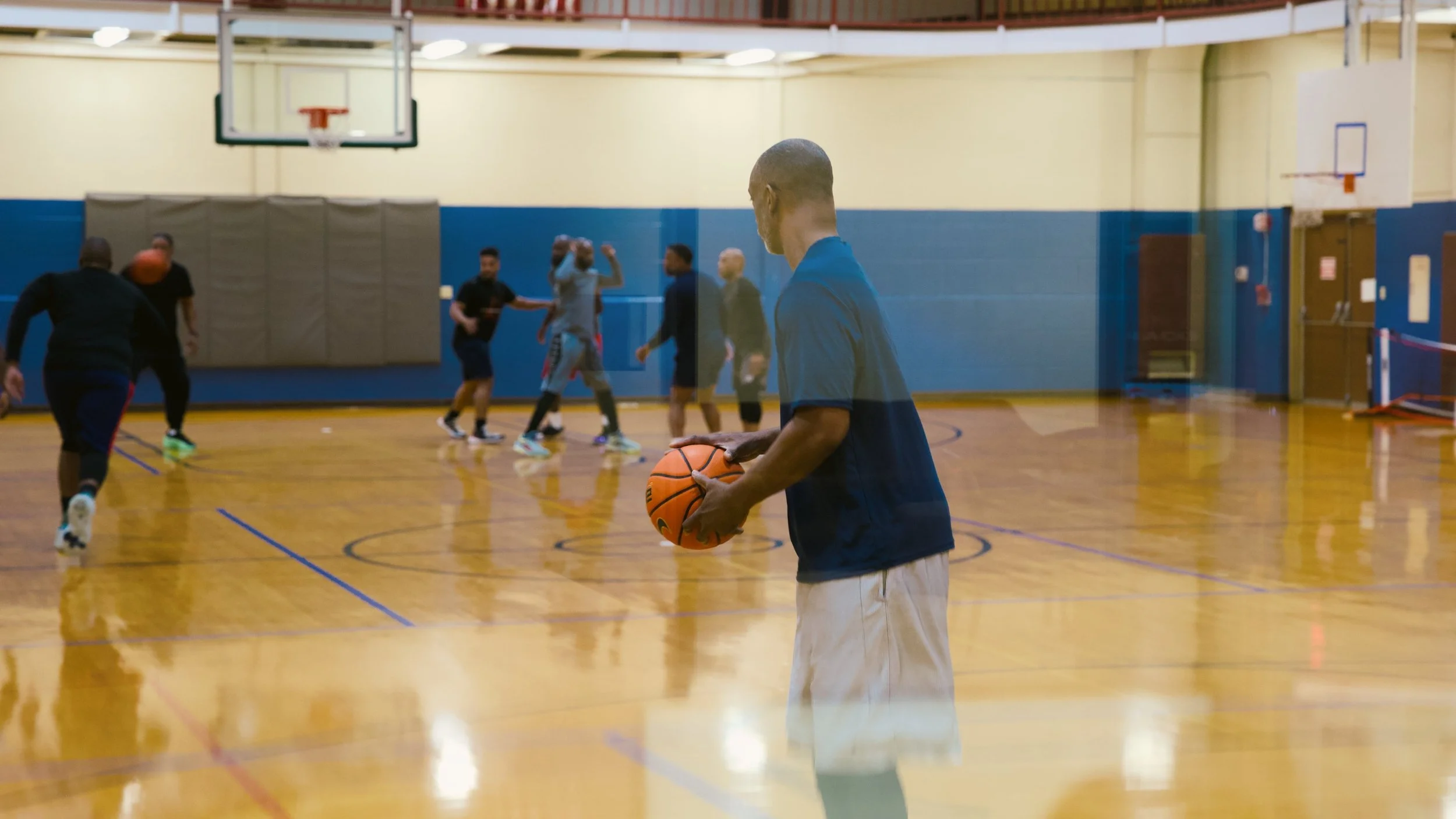 Group of men playing basketball in an indoor gym, with one man in the foreground holding a basketball.