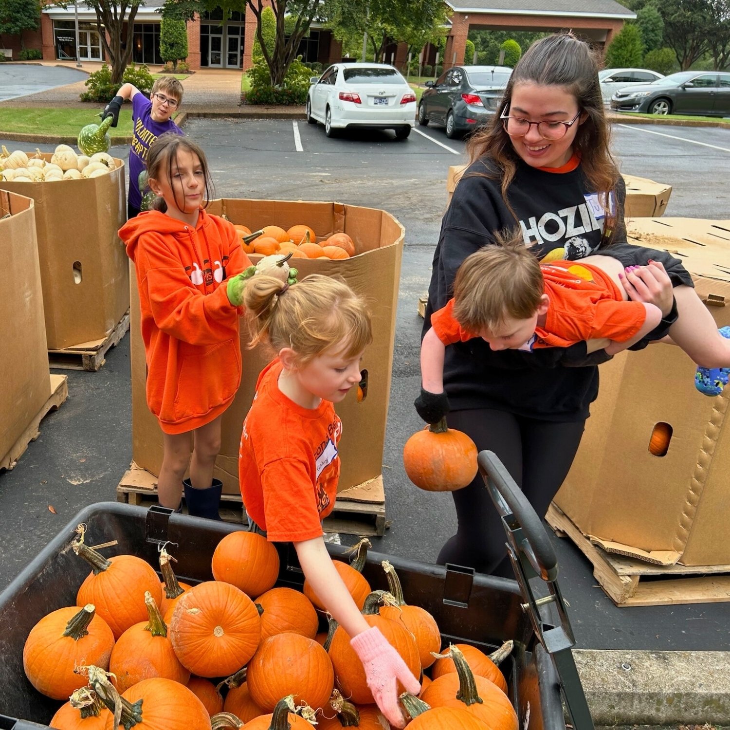 Children and a woman picking pumpkins at a pumpkin patch or farm market.