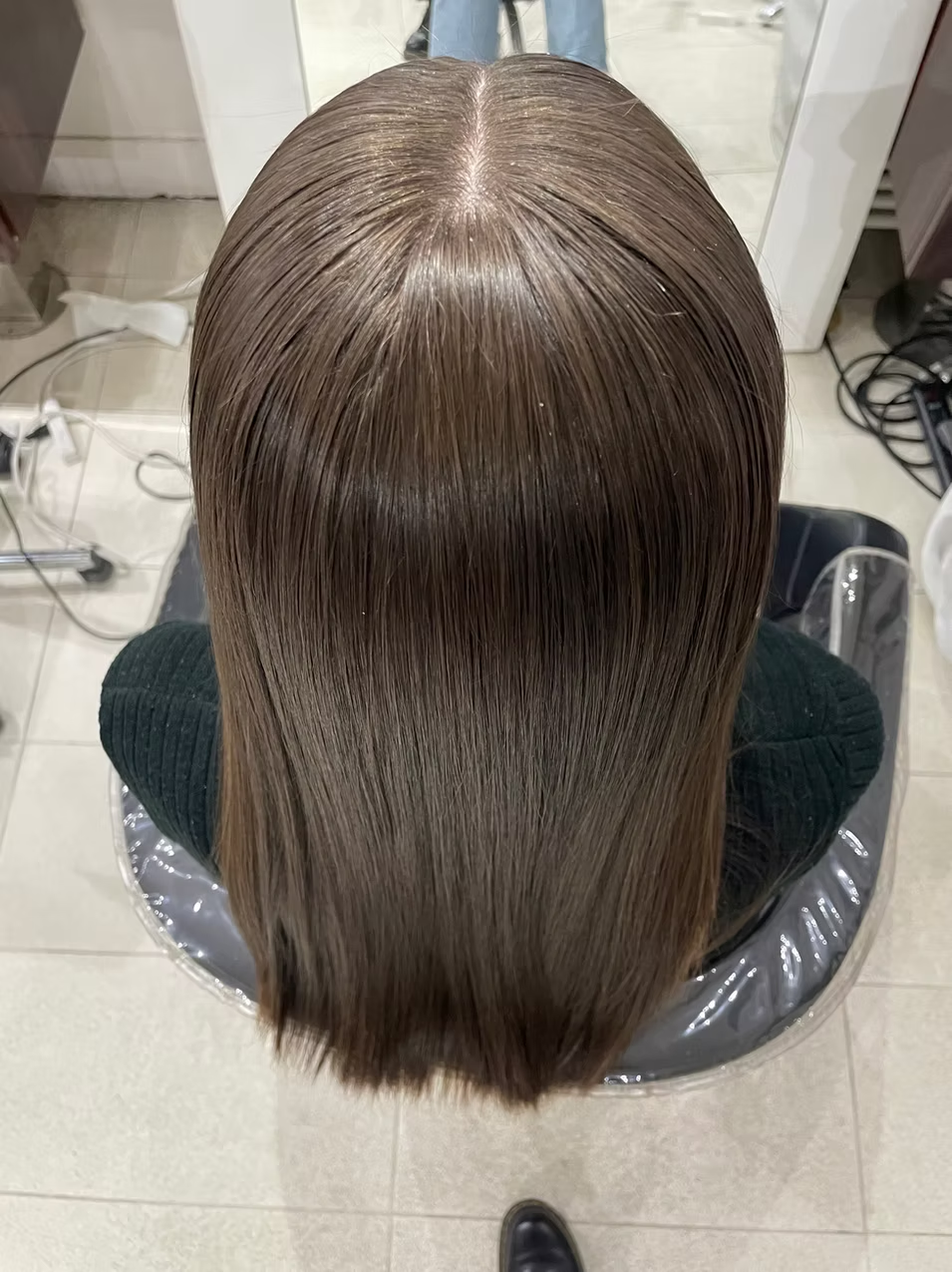 Top view of a person's shiny, straight, brown hair in a salon chair.